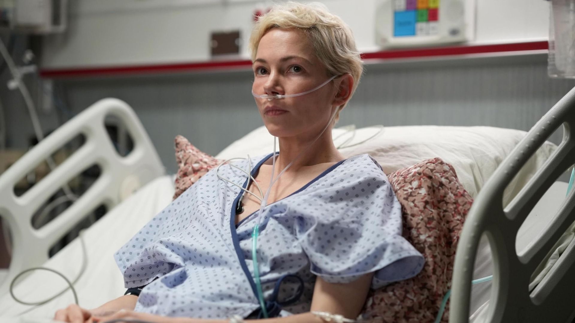 Aktorka Michelle Williams w szpitalnym ubraniu leży na łóżku z rurką w nosie