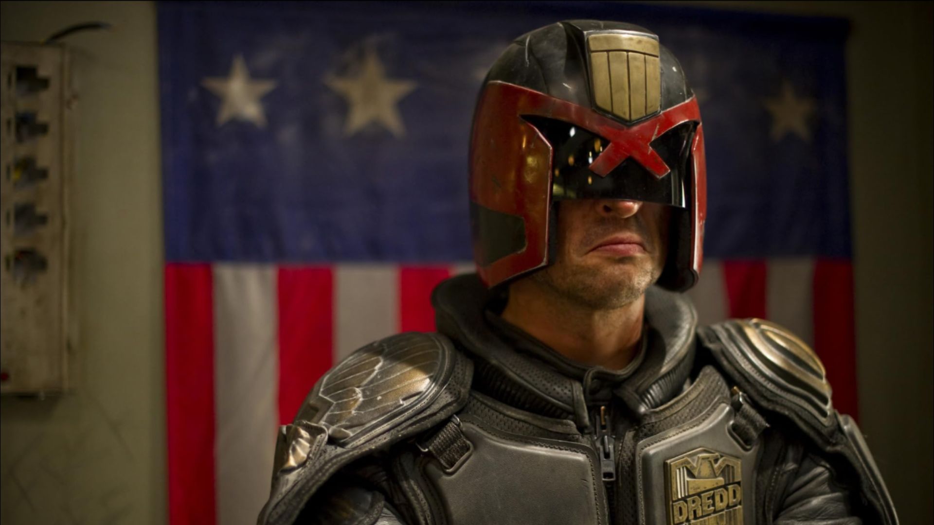 Aktor Karl Urban w szarym futurystycznym stroju i czarno-czerwonym hełmie