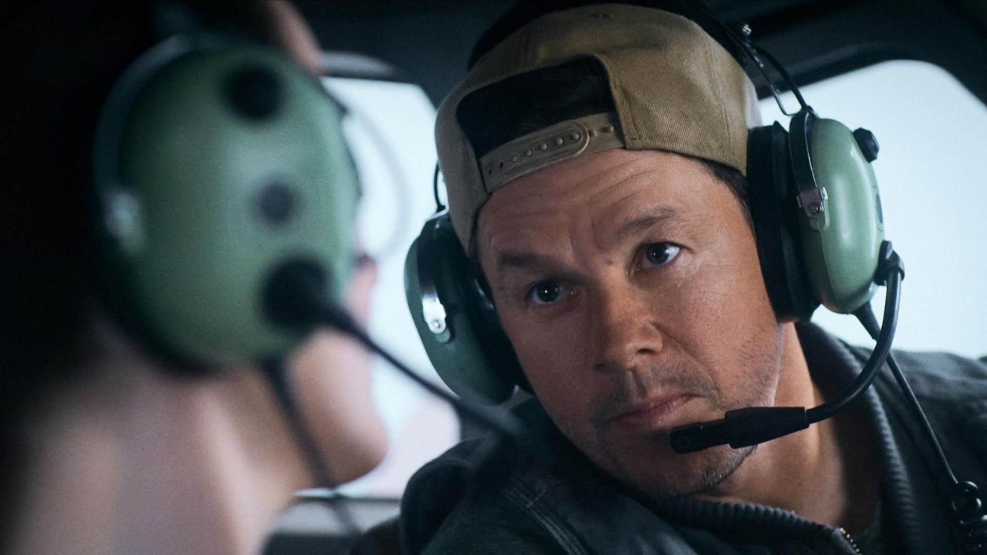Aktor Mark Wahlberg w czapce i słuchawkach z mikrofonem siedzi w samolocie