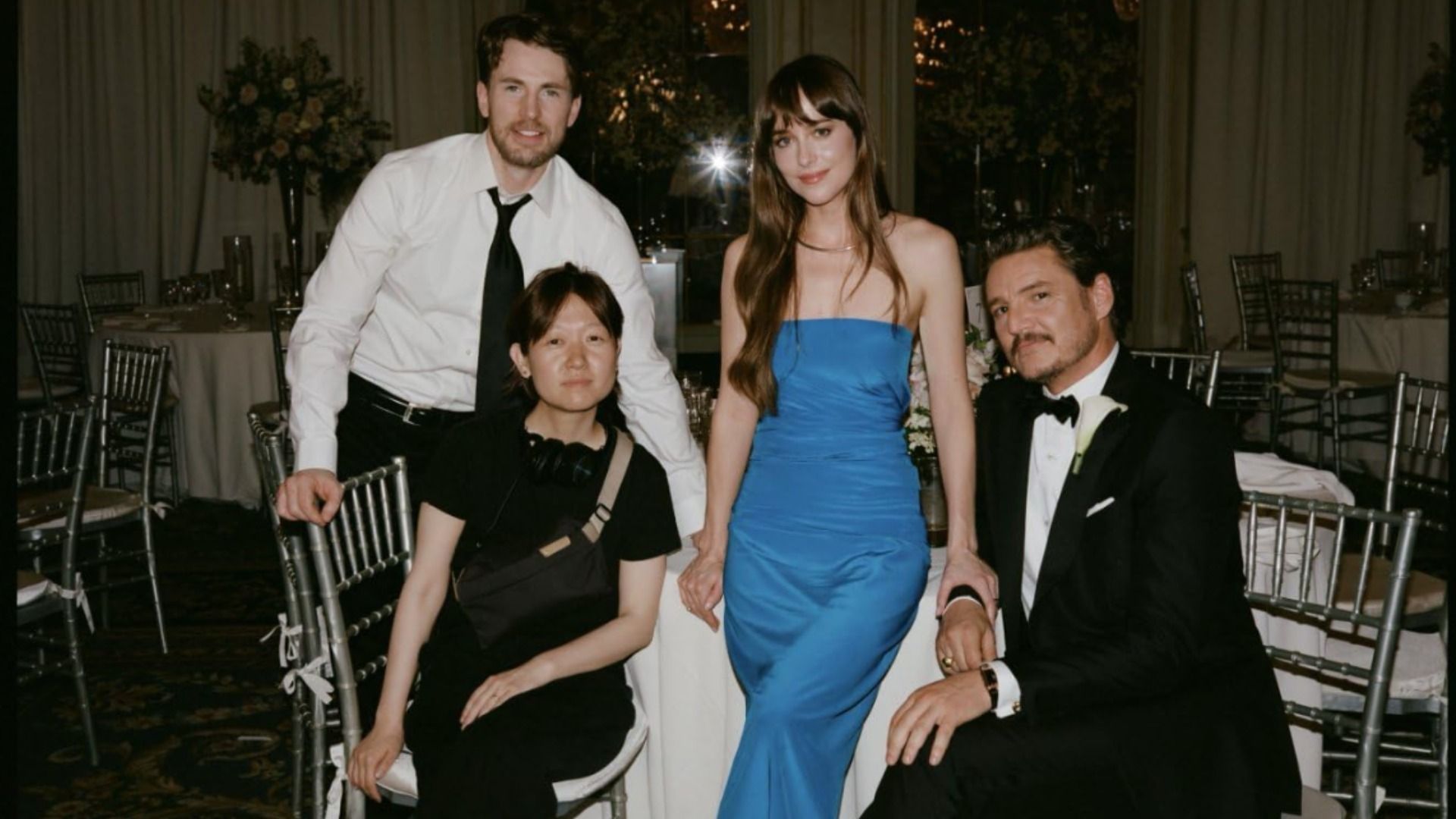 Aktorzy Dakota Johnson, Chris Evans i Pedro Pascal siedzący w wieczorowych strojach przy białym stole