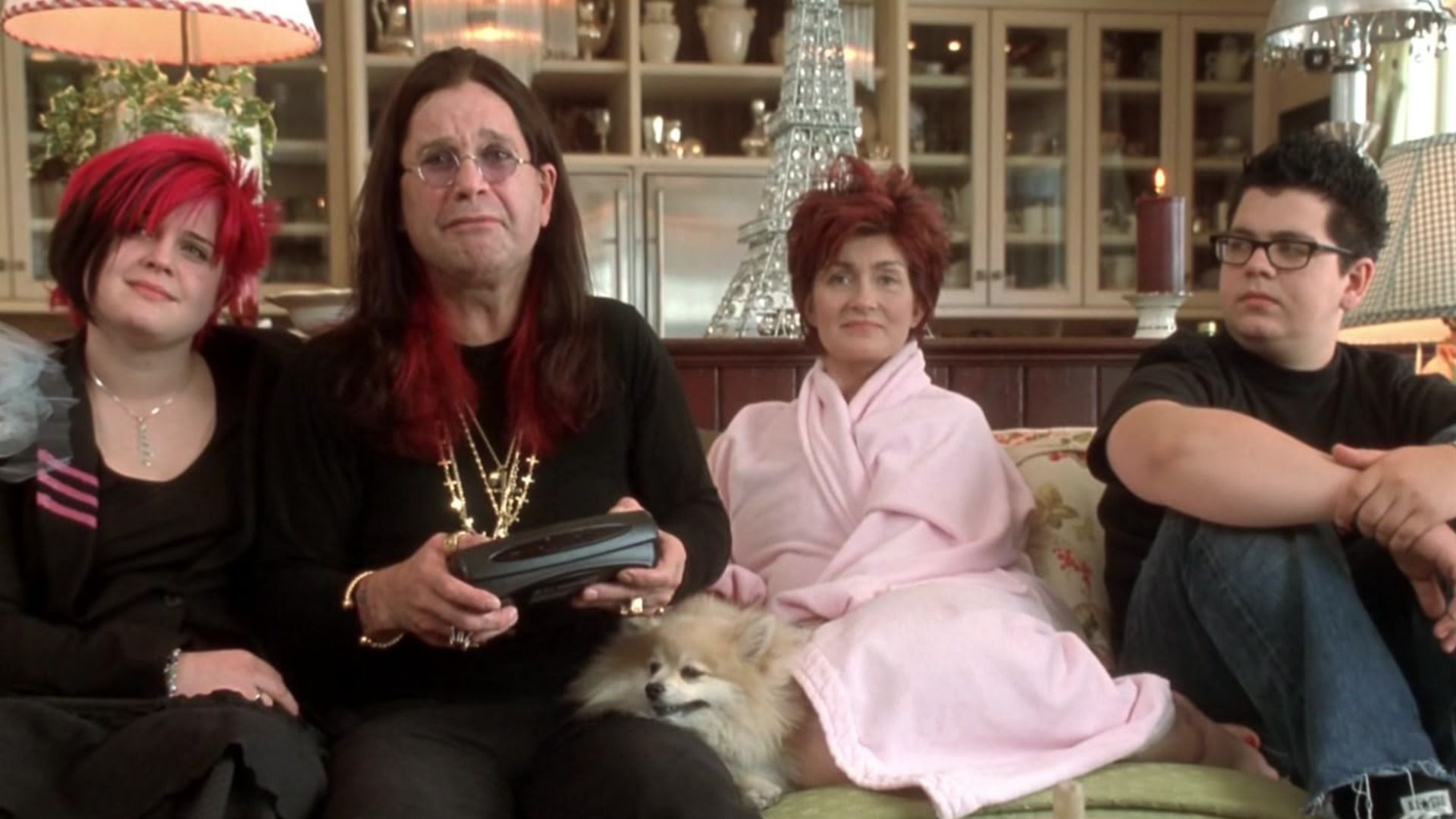 Wokalista Ozzy Osbourne w czarnym garniturze z łańcuchami siedzi na kanapie z żoną i dziećmi
