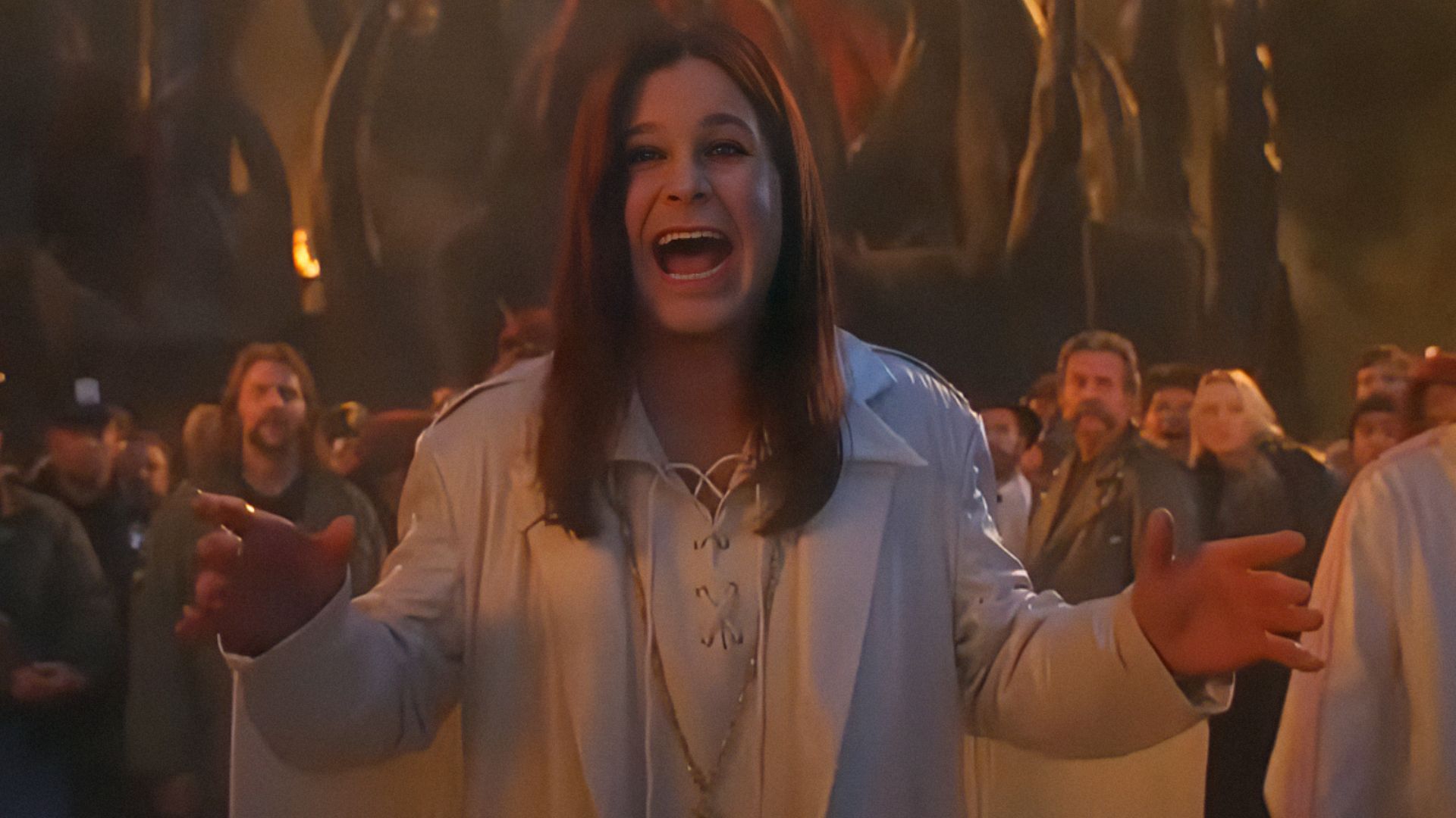 Wokalista Ozzy Osbourne w białej kurtce rozkłada szeroko ramiona i uśmiecha się