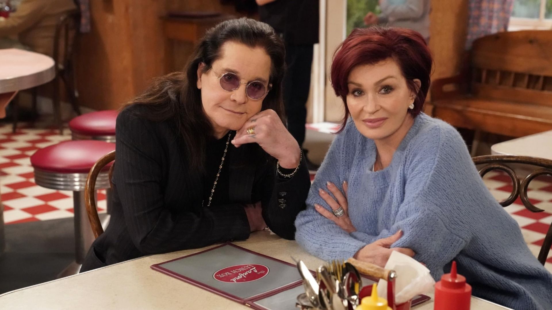 Wokalista Ozzy Osbourne w okularach i czarnej kurtce siedzi przy stole z żoną