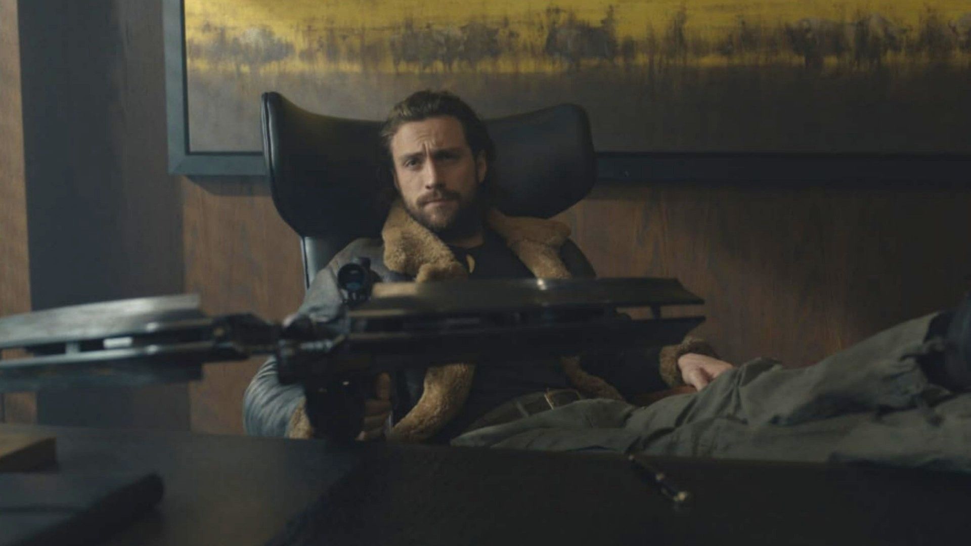 Aktor Aaron Taylor-Johnson siedzi przy stole z kuszą w rękach