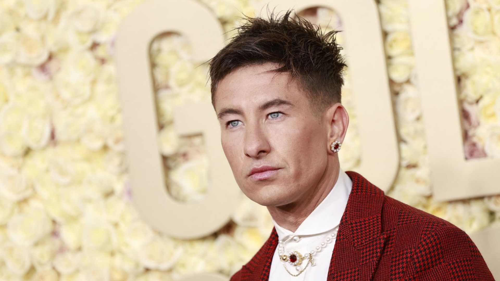 Aktor Barry Keoghan w czerwonej kurtce z kolczykiem stojący na żółtym tle