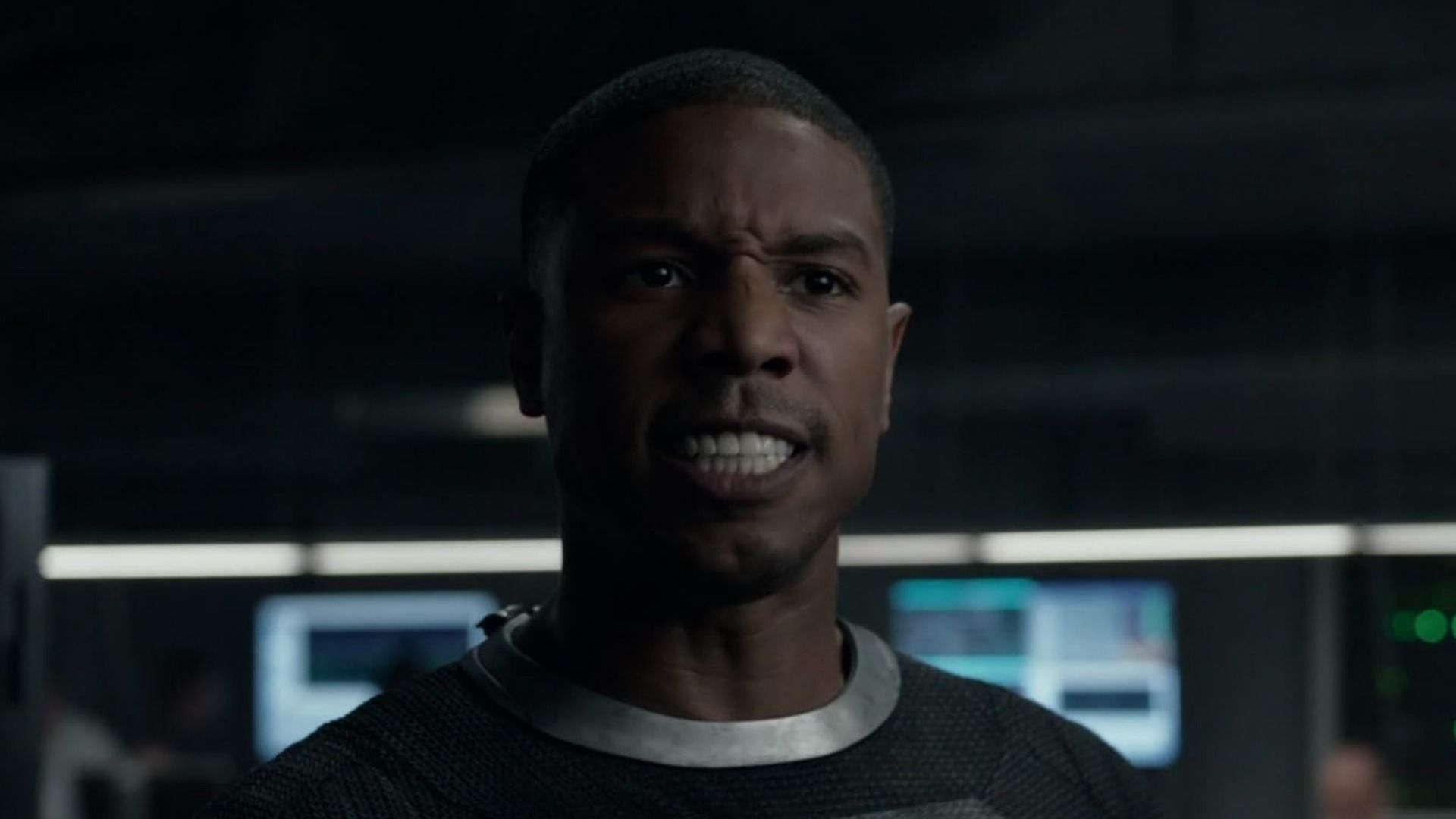 Aktor Michael B. Jordan w szarym garniturze ze złym wyrazem twarzy na rozmytym tle