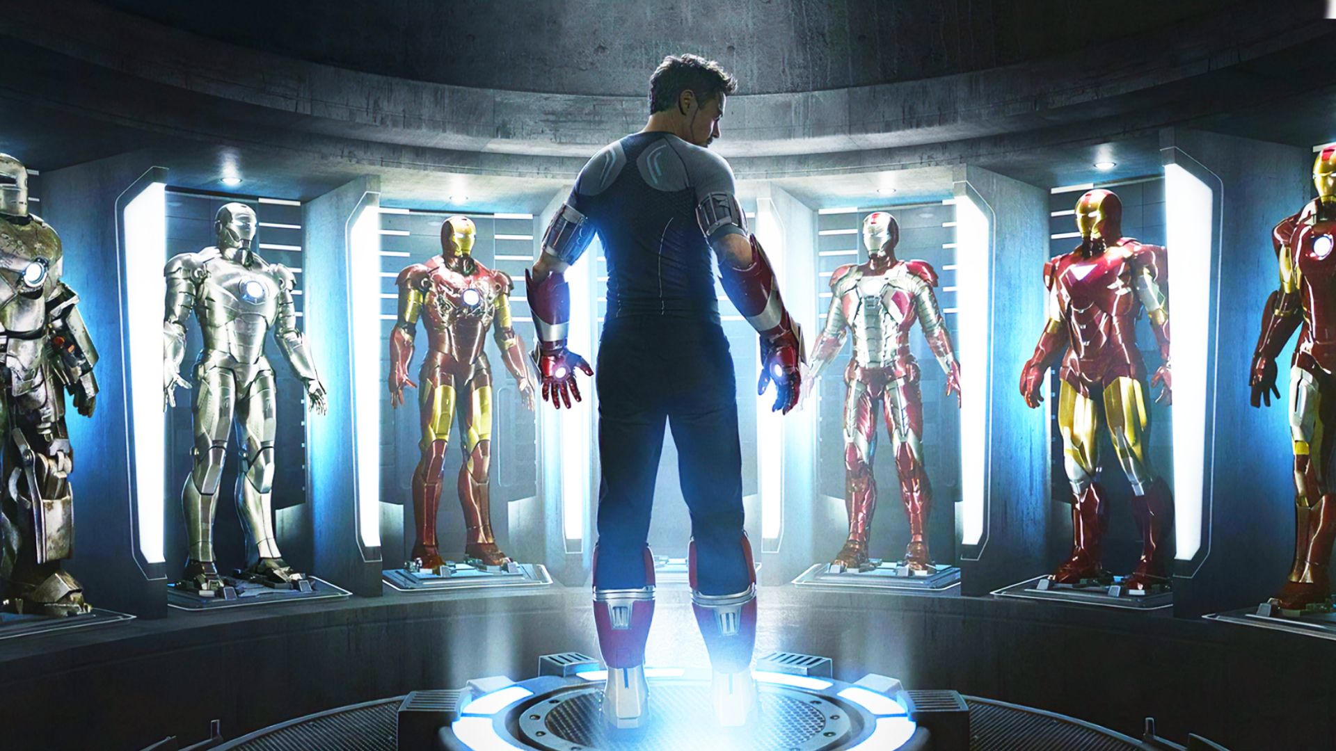 Aktor Robert Downey Jr. w szaro-czarnym ubraniu stoi otoczony zbrójami Iron Mana