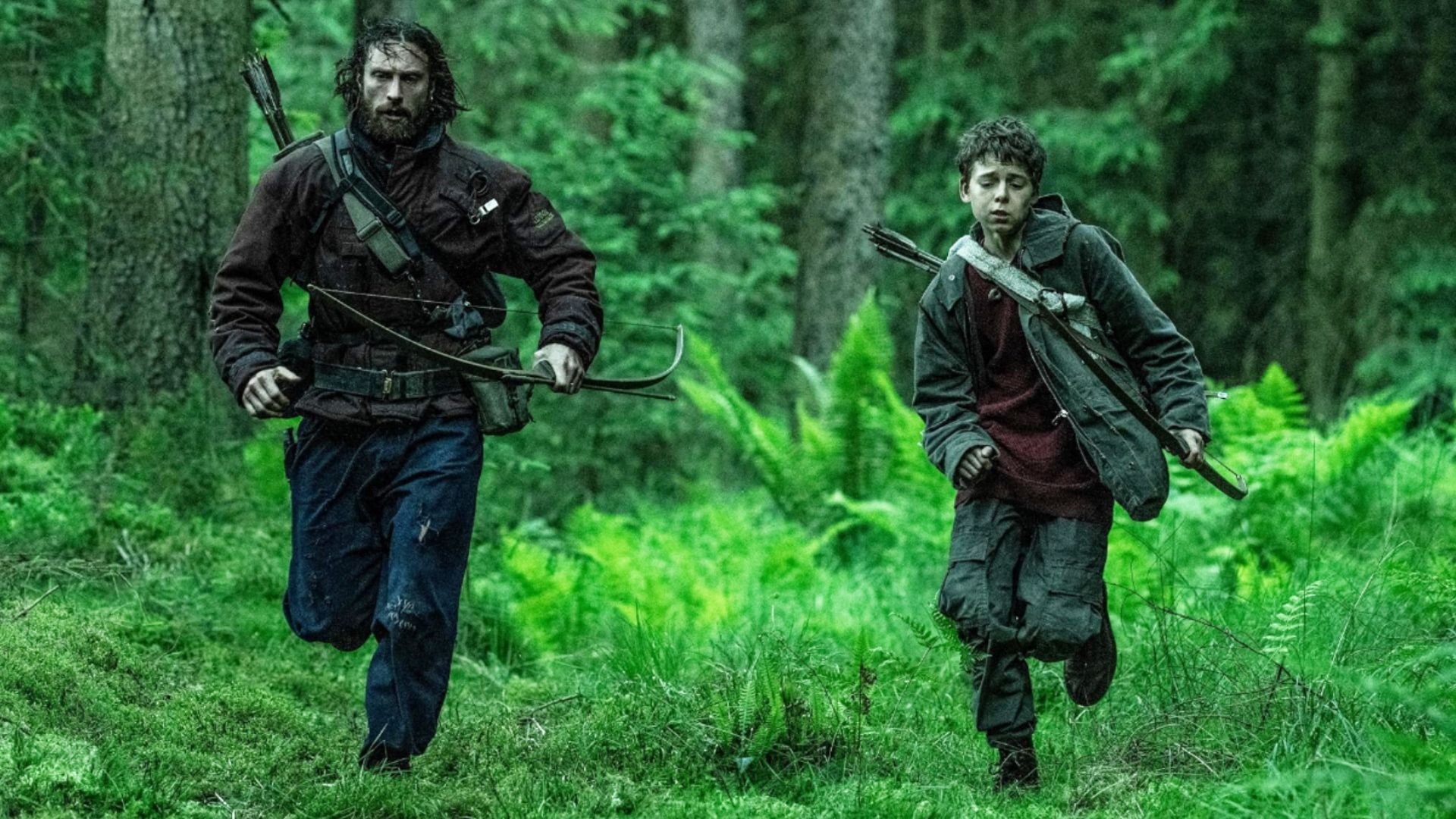 Aktor Aaron Taylor-Johnson w brudnych ubraniach biega przez las obok dziecka z łukiem
