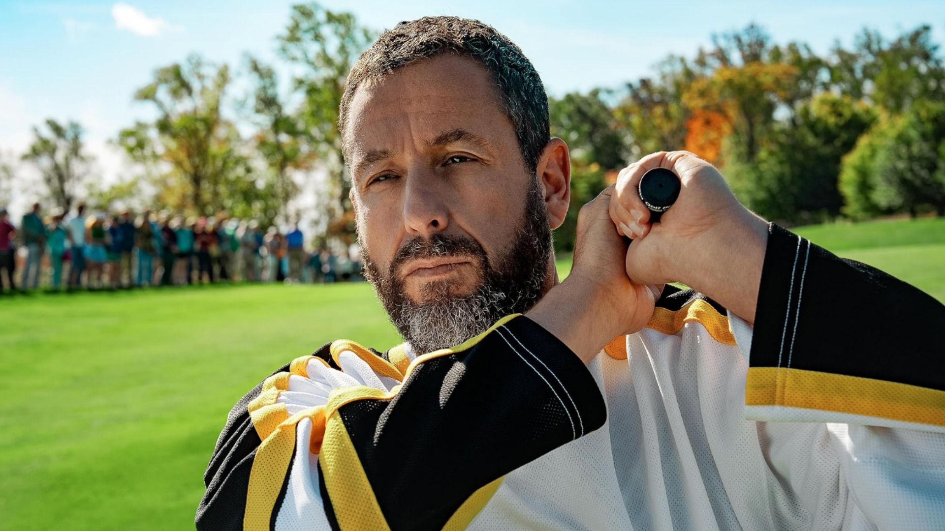 Aktor Adam Sandler trzymający kij golfowy stojący na polu golfowym