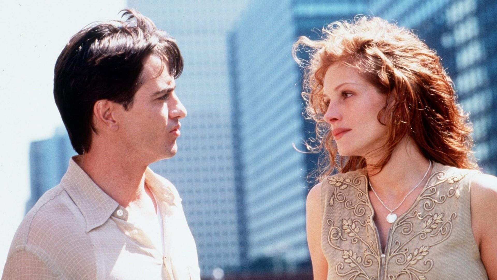 Aktor Dermot Mulroney w jasnej koszuli patrzy na aktorkę Julię Roberts na tle wysokich budynków