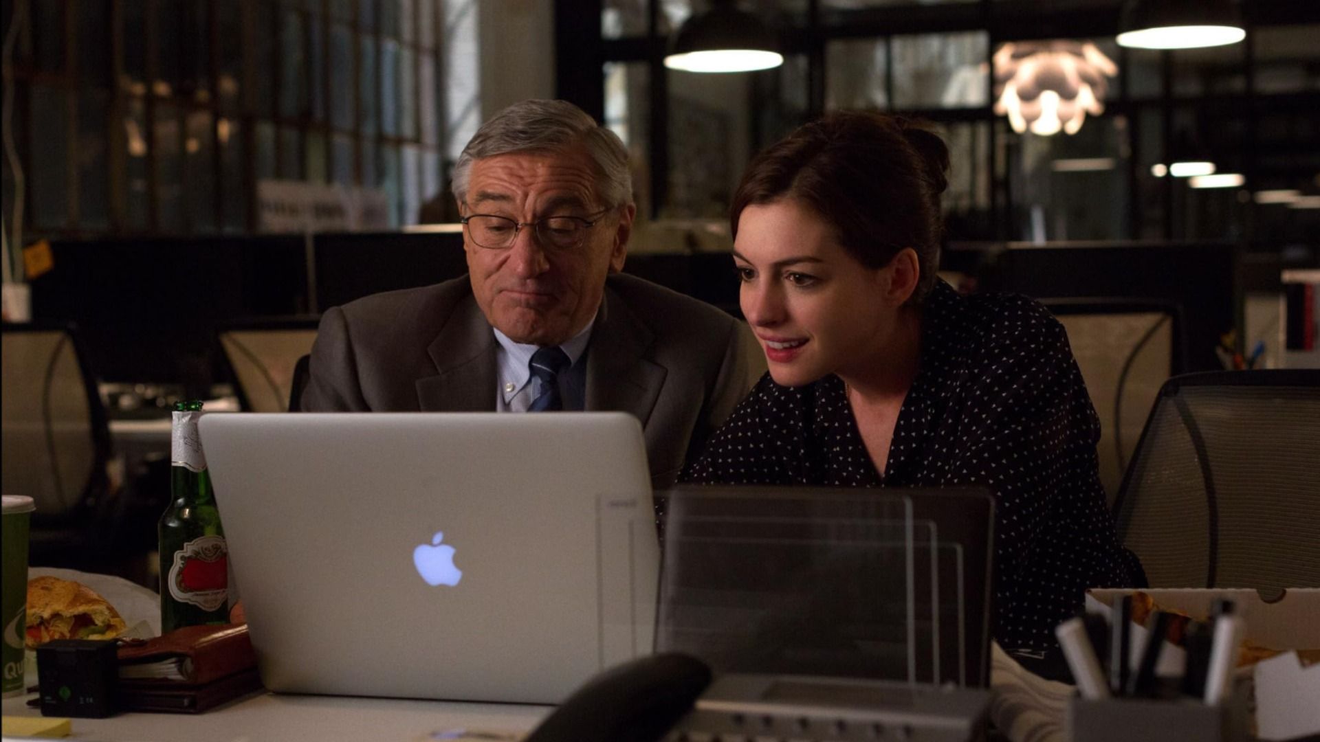 Aktor Robert De Niro w szarym żakiecie i aktorka Anne Hathaway w czarnej sukience siedzą przy stole