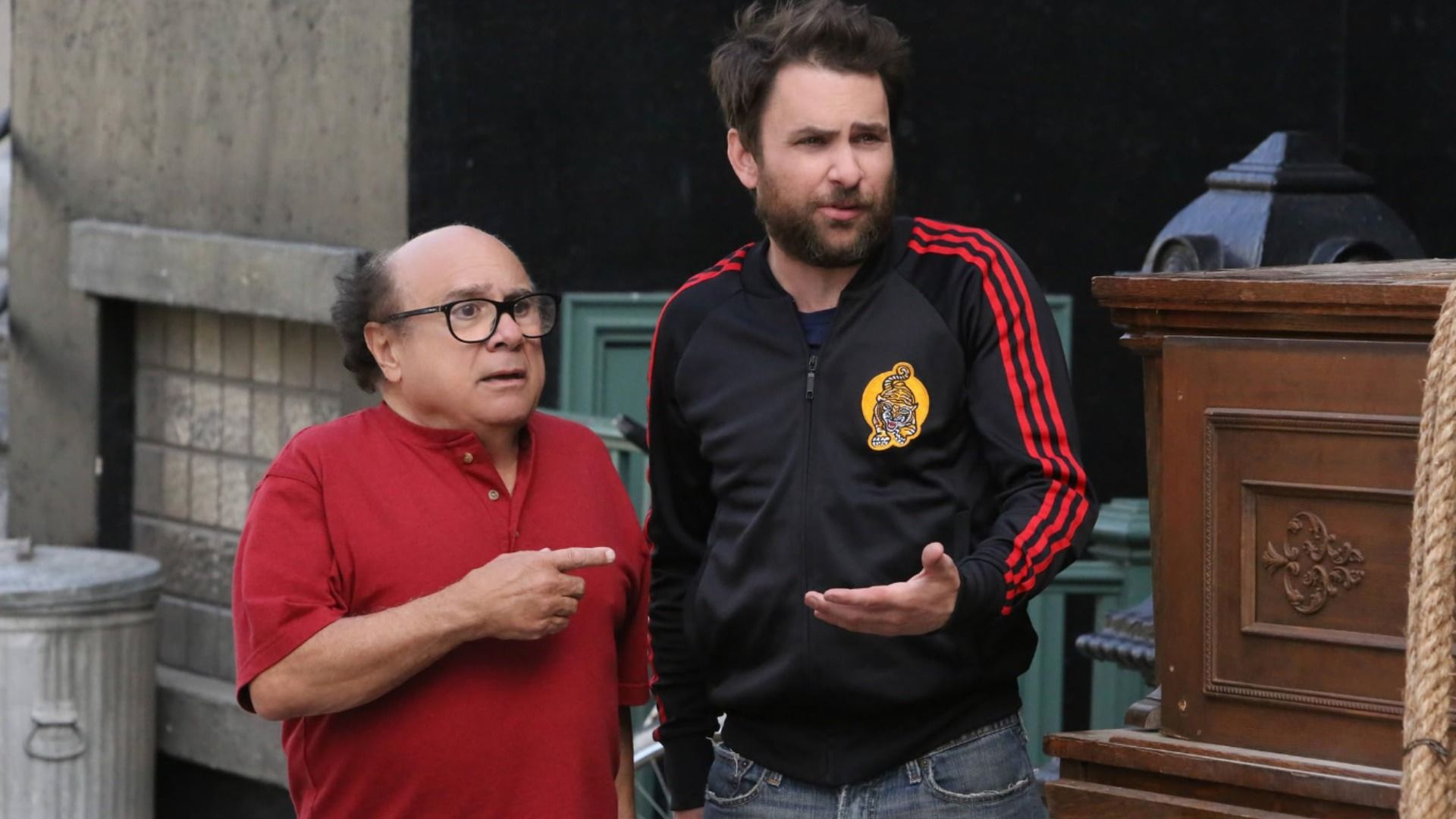Aktor Danny DeVito w czerwonej koszuli wskazuje palcem na mężczyznę w stroju sportowym