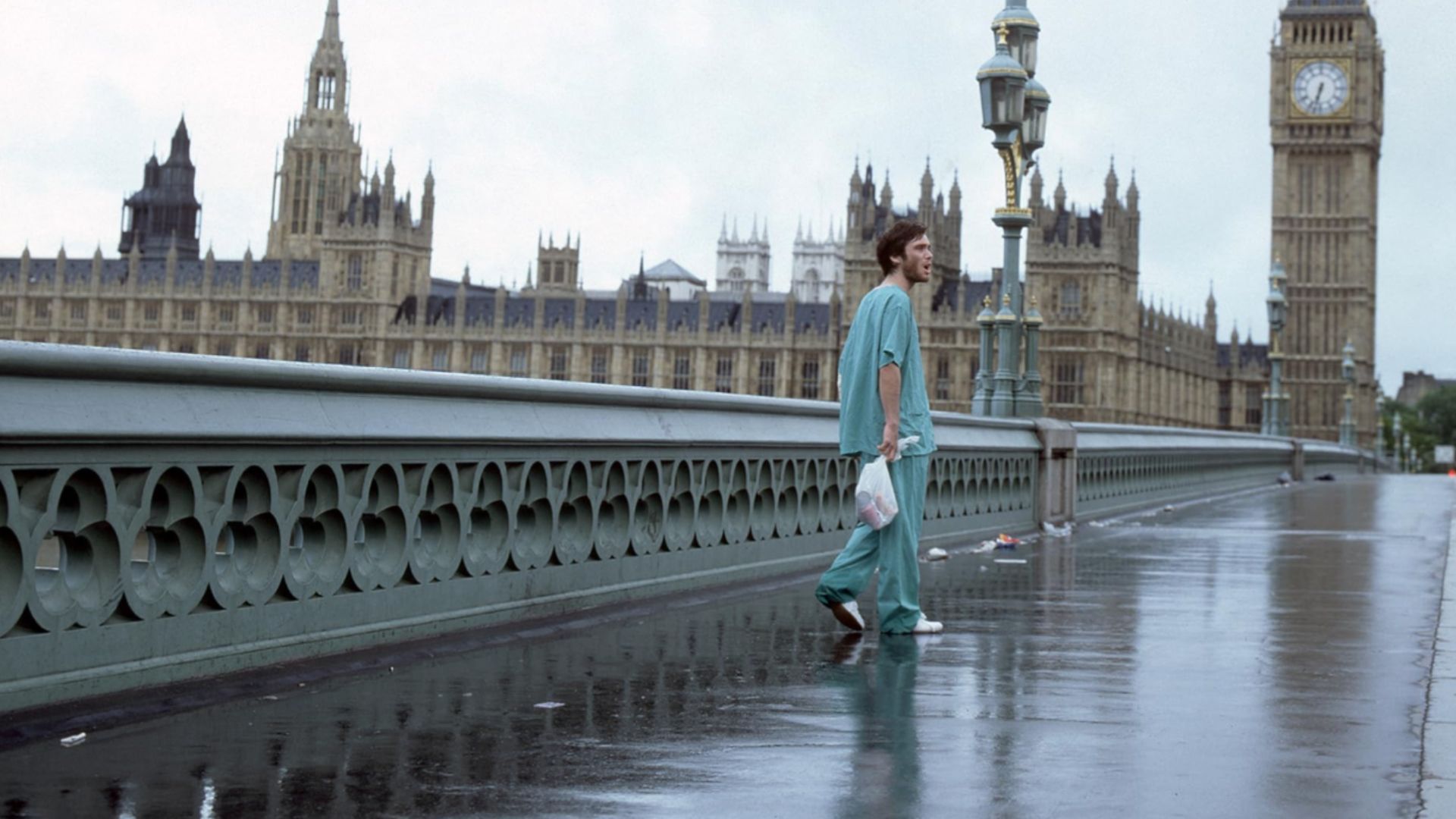 Aktor Cillian Murphy w niebieskim ubraniu stoi na pustym moście z widoczną w pobliżu londyńską wieżą zegarową Big Ben