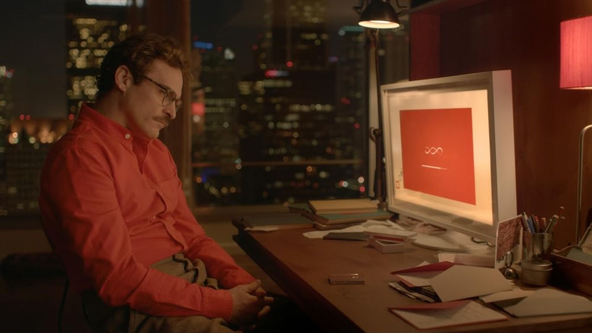 Aktor Joaquin Phoenix w czerwonej koszuli siedzi przy stole z komputerem