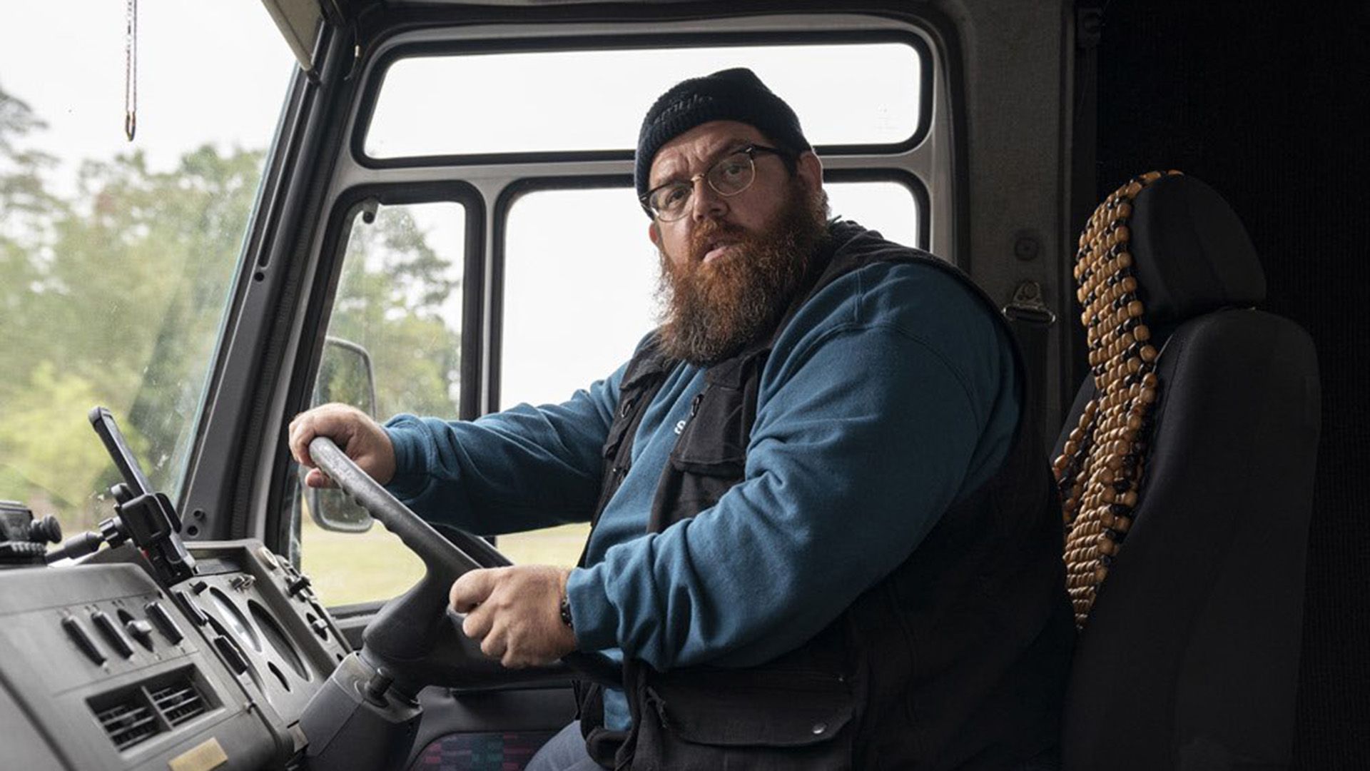 Nick Frost w okularach i kapeluszu siedzi za kierownicą ciężarówki, patrząc w kamerę