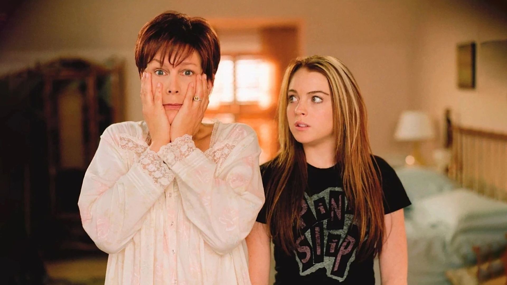Jamie Lee Curtis w piżamie zszokowana z rękami zakrywającymi twarz, podczas gdy Lindsay Lohan patrzy na nią ze zdziwieniem