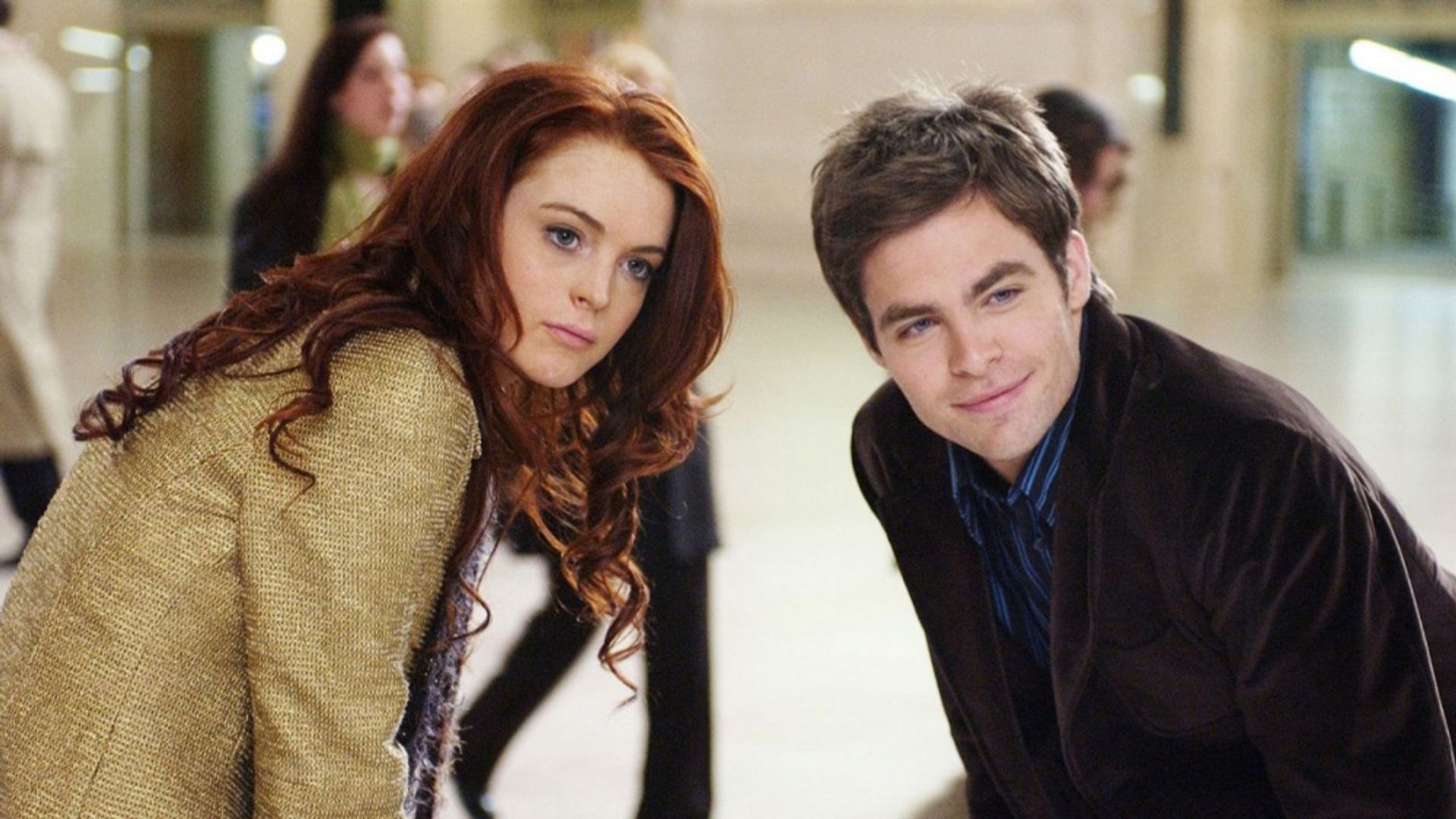 Lindsay Lohan i Chris Pine stoją obok siebie, pochylając się do przodu w zatłoczonym pomieszczeniu
