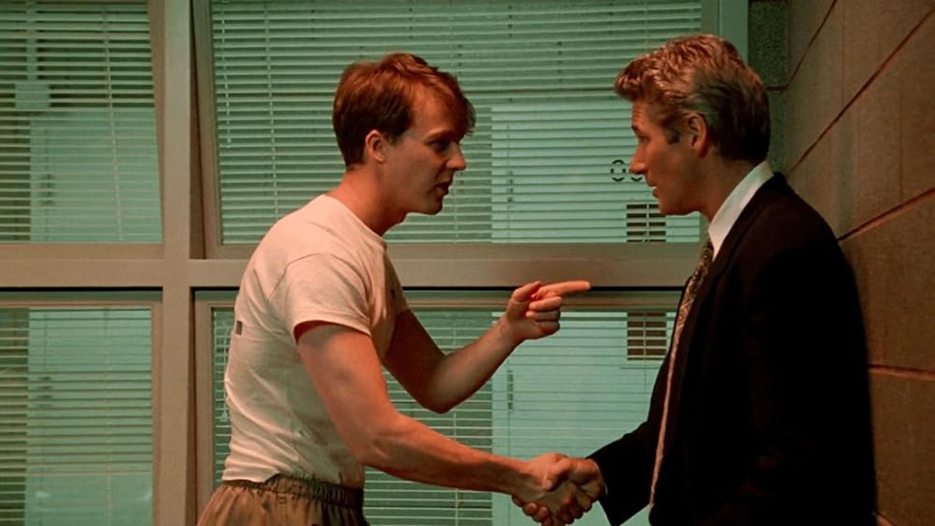 Edward Norton w koszulce podaje rękę Richardowi Gere'owi w garniturze, wskazując na niego palcem