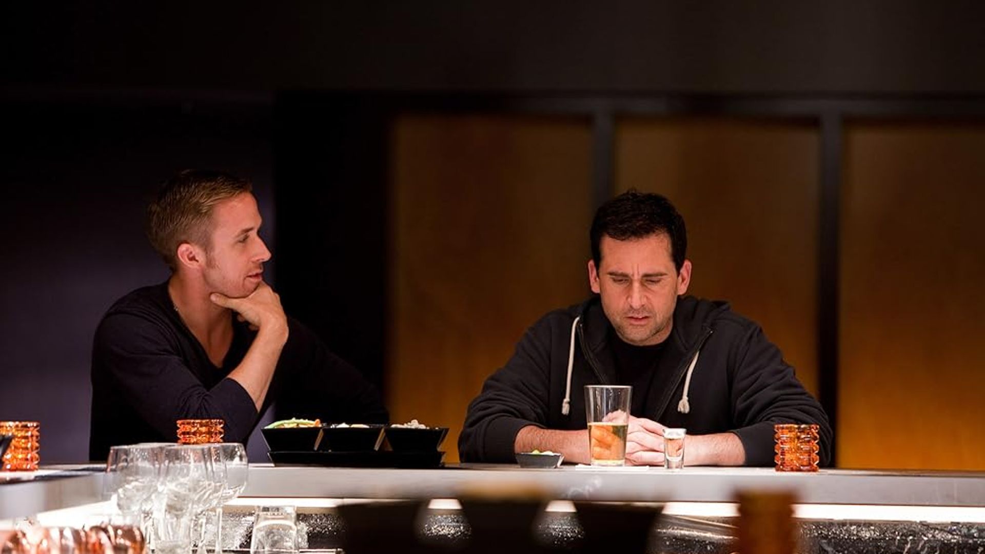 Ryan Gosling i Steve Carell siedzą przy barowym blacie, jeden wpatruje się zamyślony w szklankę, drugi obserwuje