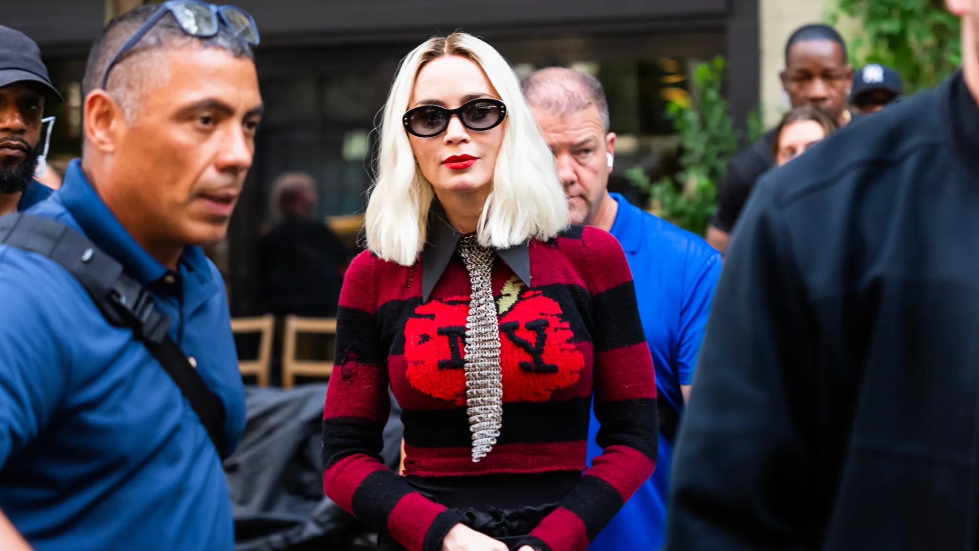 Emily Blunt z platynowym bobem w czerwonym swetrze z napisem NY