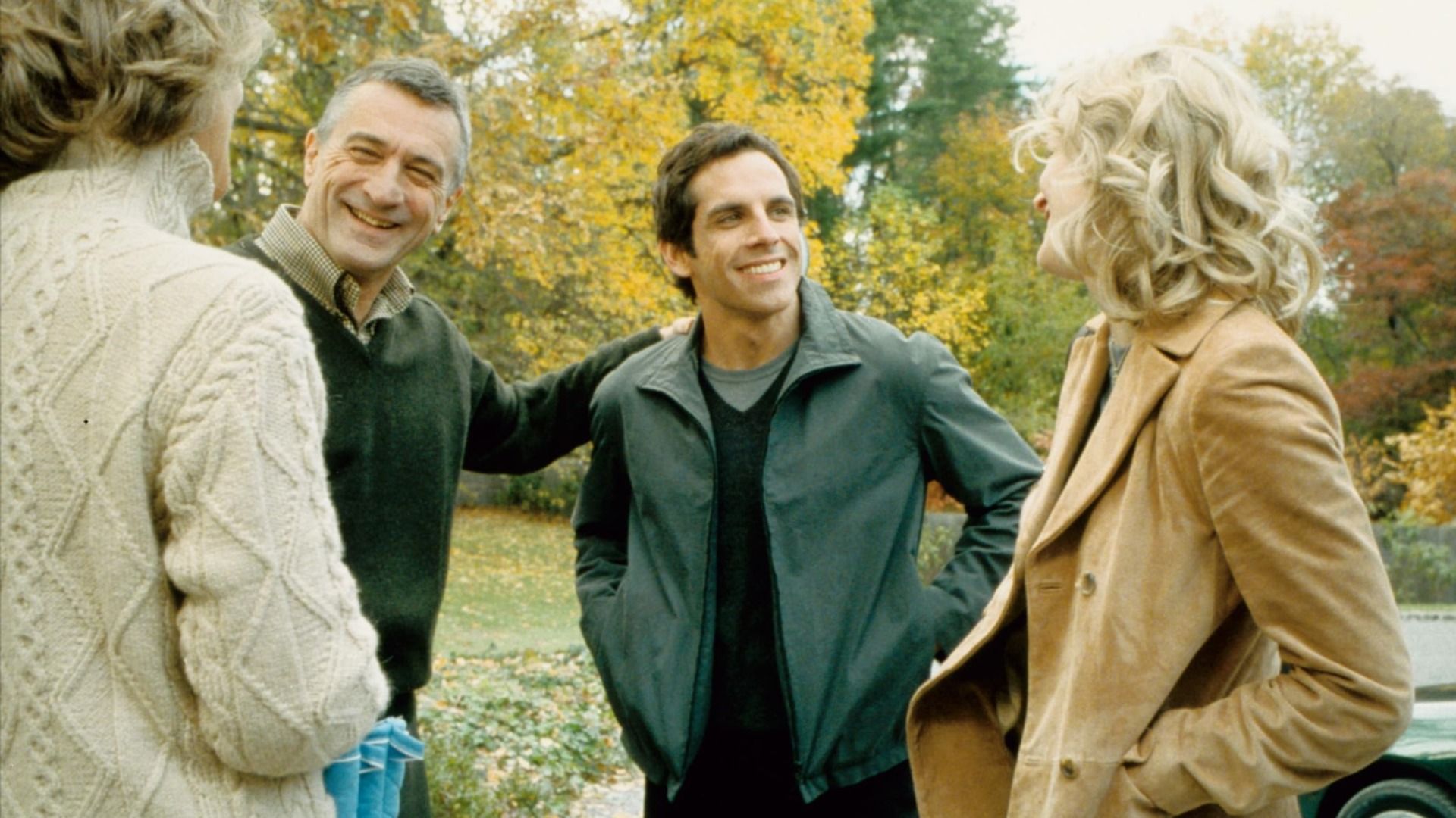 Aktorzy Robert De Niro w zielonym swetrze i Ben Stiller w zielonej kurtce stojący obok drzew z żółtymi liśćmi