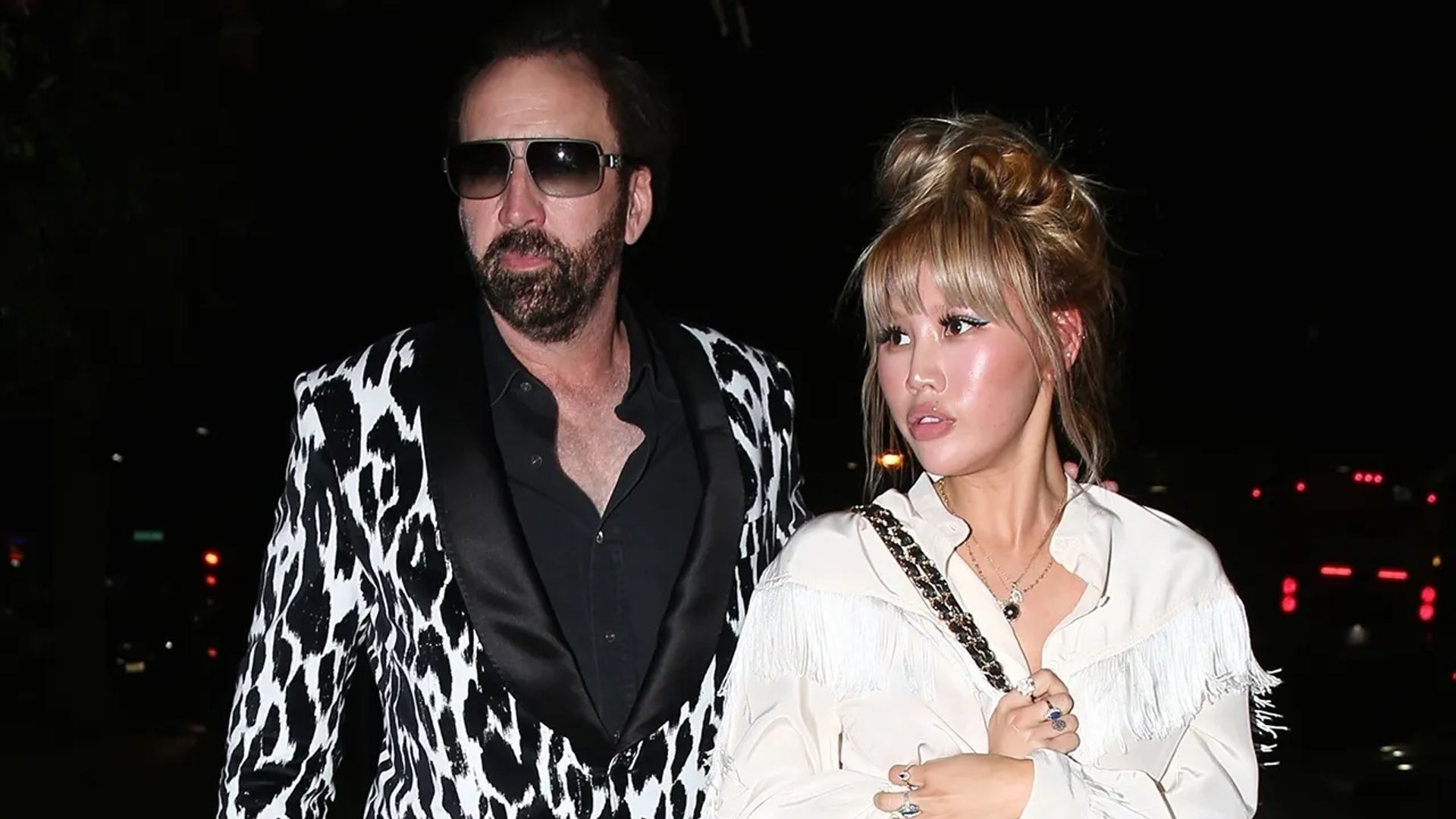 Nicolas Cage w czarno-białej wzorzystej marynarce i Erika Koike w białej bluzce idący razem nocą