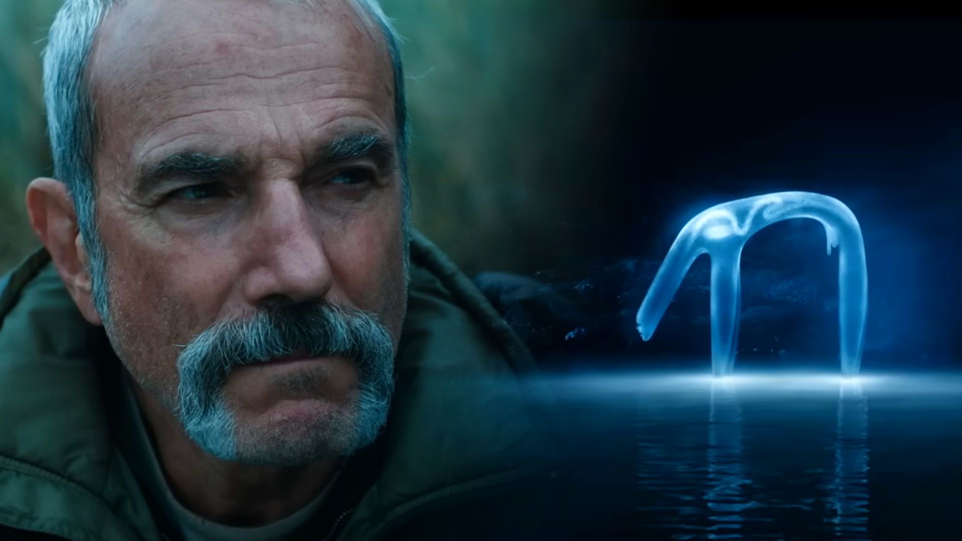 Aktor Daniel Day-Lewis w zielonej kurtce i półprzezroczyste niebieskawe stworzenie stojące na wodzie