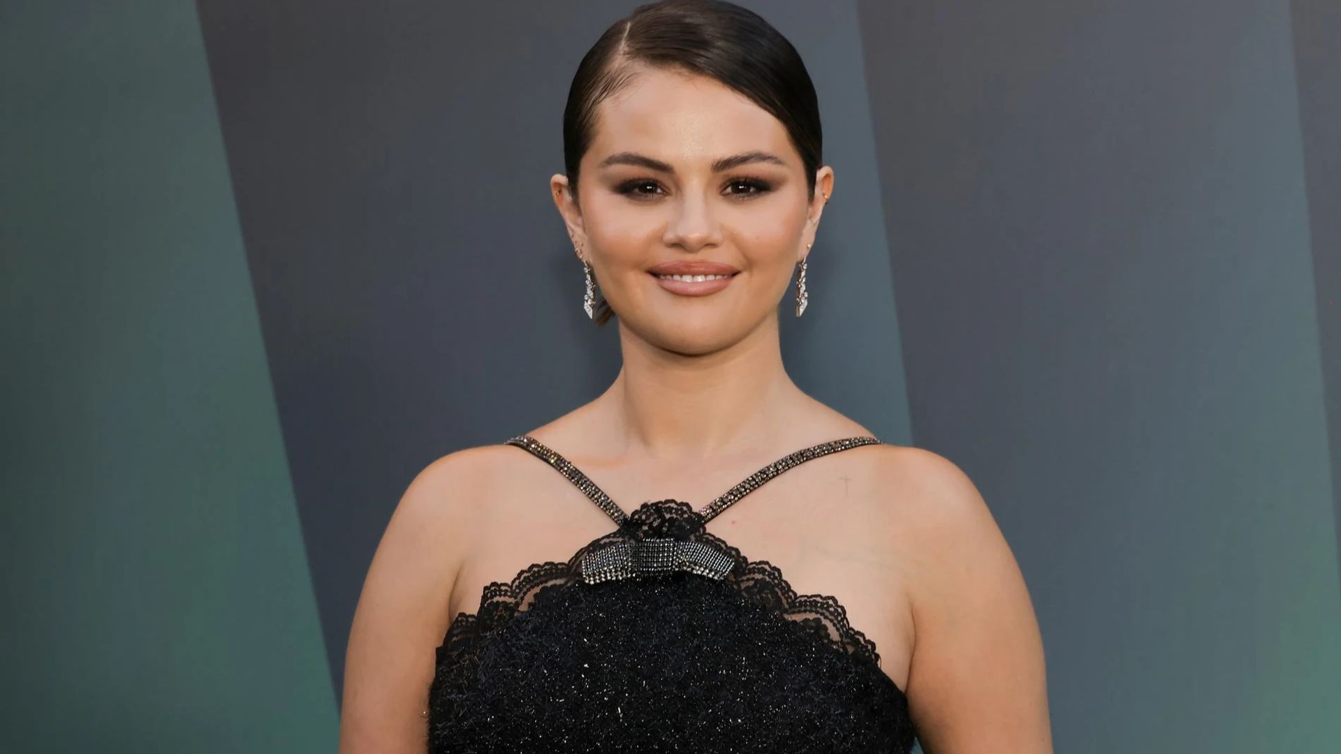 Selena Gomez w czarnej sukience pozuje do kamer z delikatnym uśmiechem