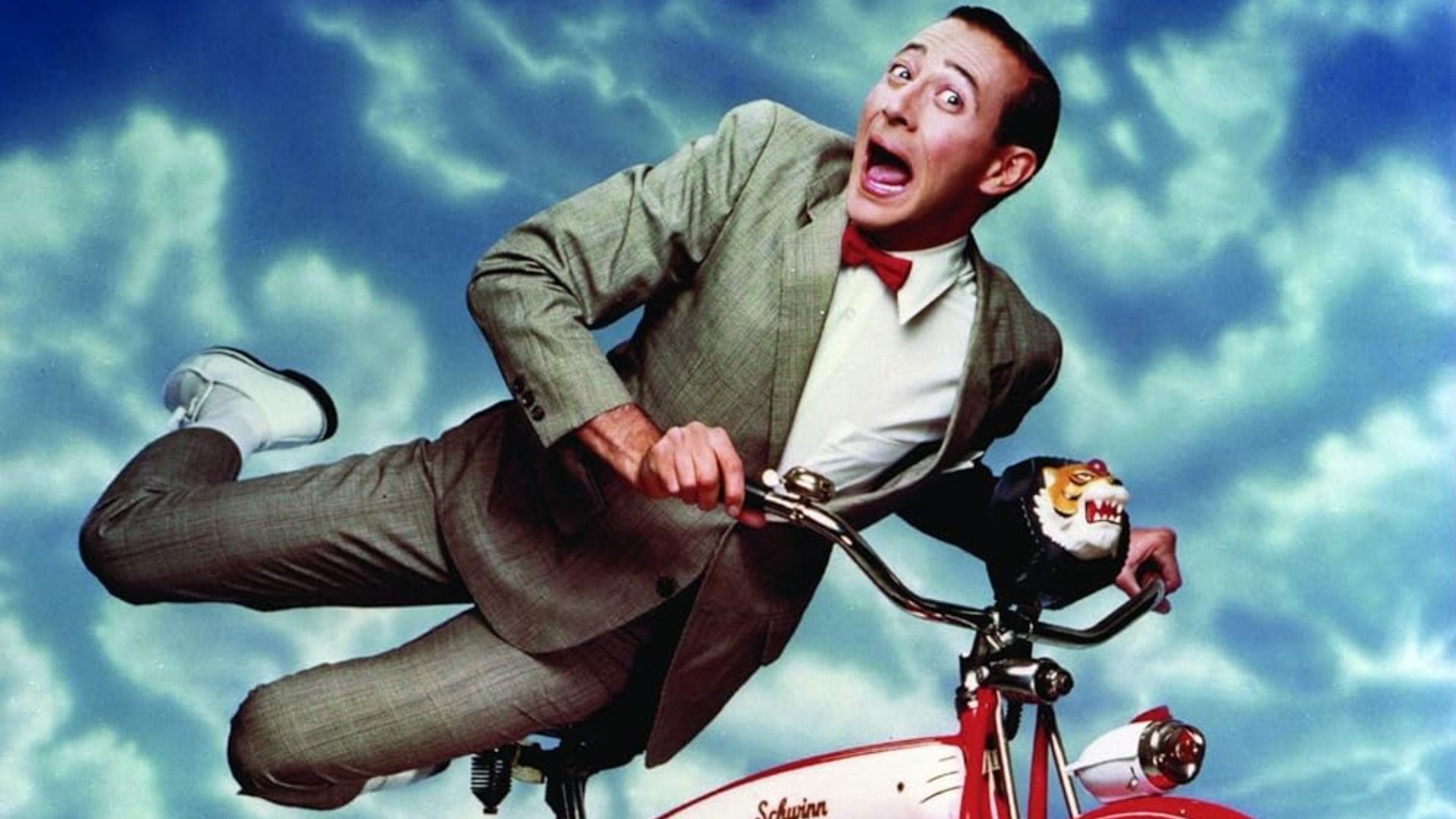 Aktor i komik Paul Reubens w szarym garniturze na rowerze
