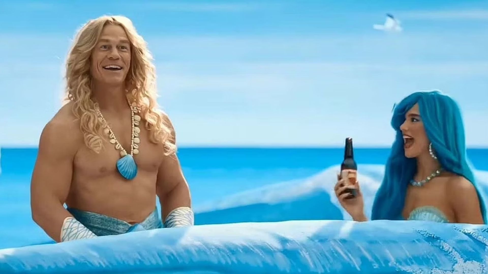 John Cena i Dua Lipa w kostiumach syren płynących przez malowane fale
