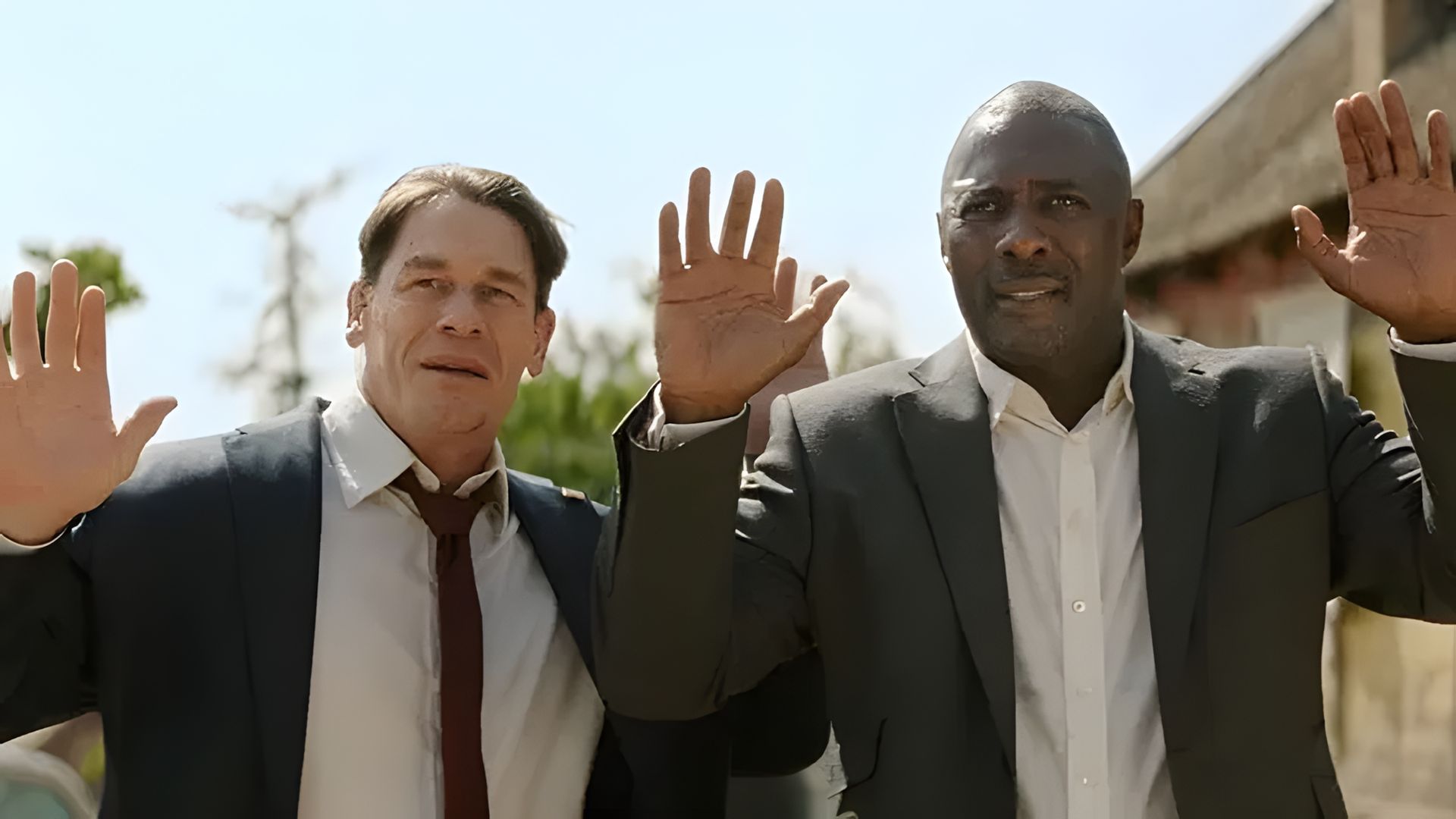 John Cena i Idris Elba w garniturach podnoszący ręce do góry, scena z filmu akcji