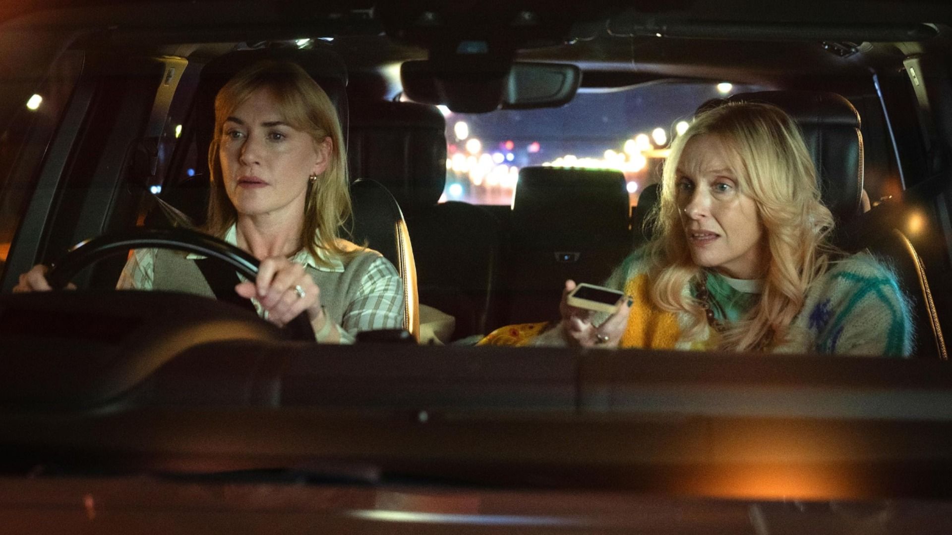 Aktorka Kate Winslet siedzi za kierownicą samochodu, podczas gdy aktorka Toni Collette rozmawia przez telefon obok niej