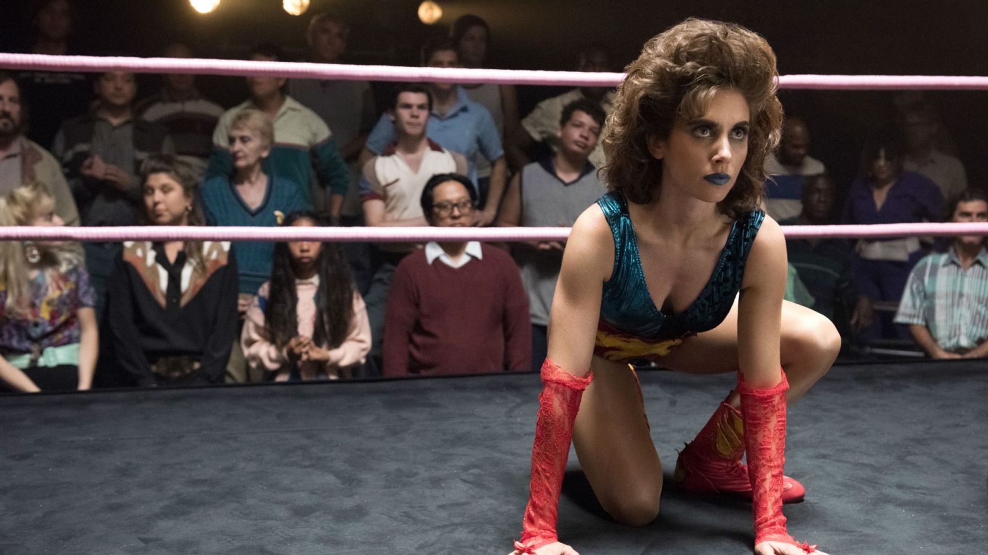 Alison Brie w stroju wrestlerki siedzi w pozycji na ringu