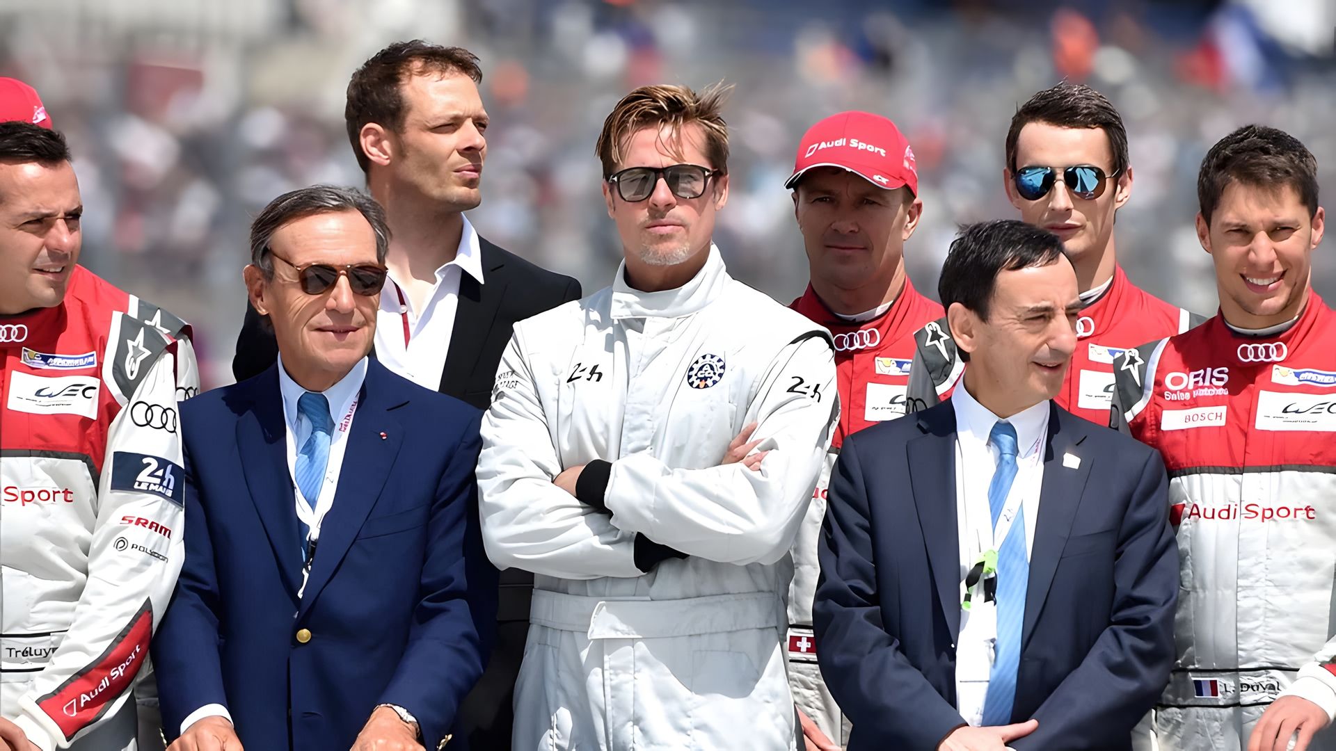 Brad Pitt w stroju kierowcy wyścigowego stoi w otoczeniu swojego zespołu