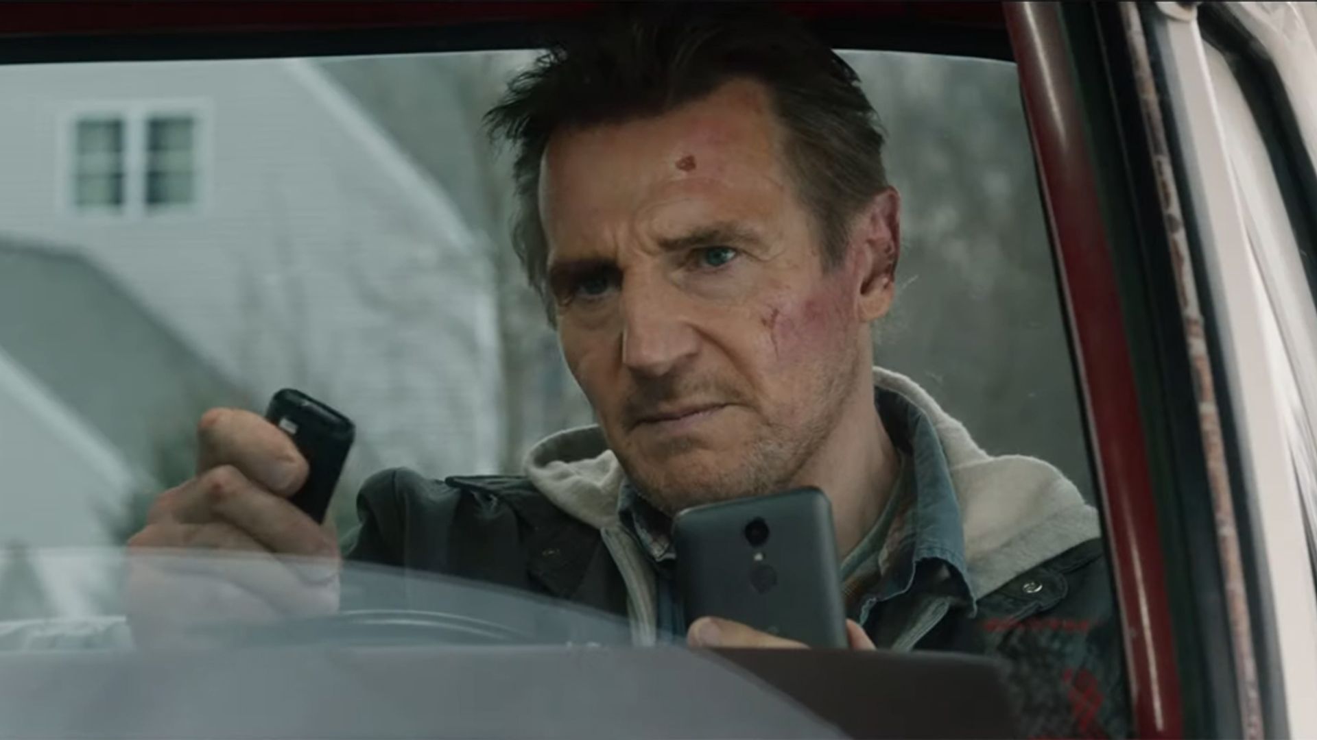 Liam Neeson siedzi w samochodzie, napięcie wpatrując się w telefon i pilota w swoich rękach