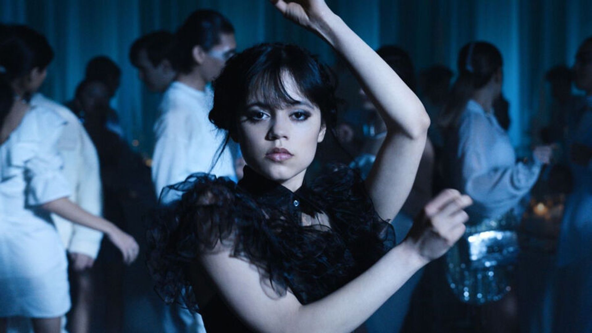 Jenna Ortega tańczy w czarnej sukience wykonując kanciate ruchy ramionami