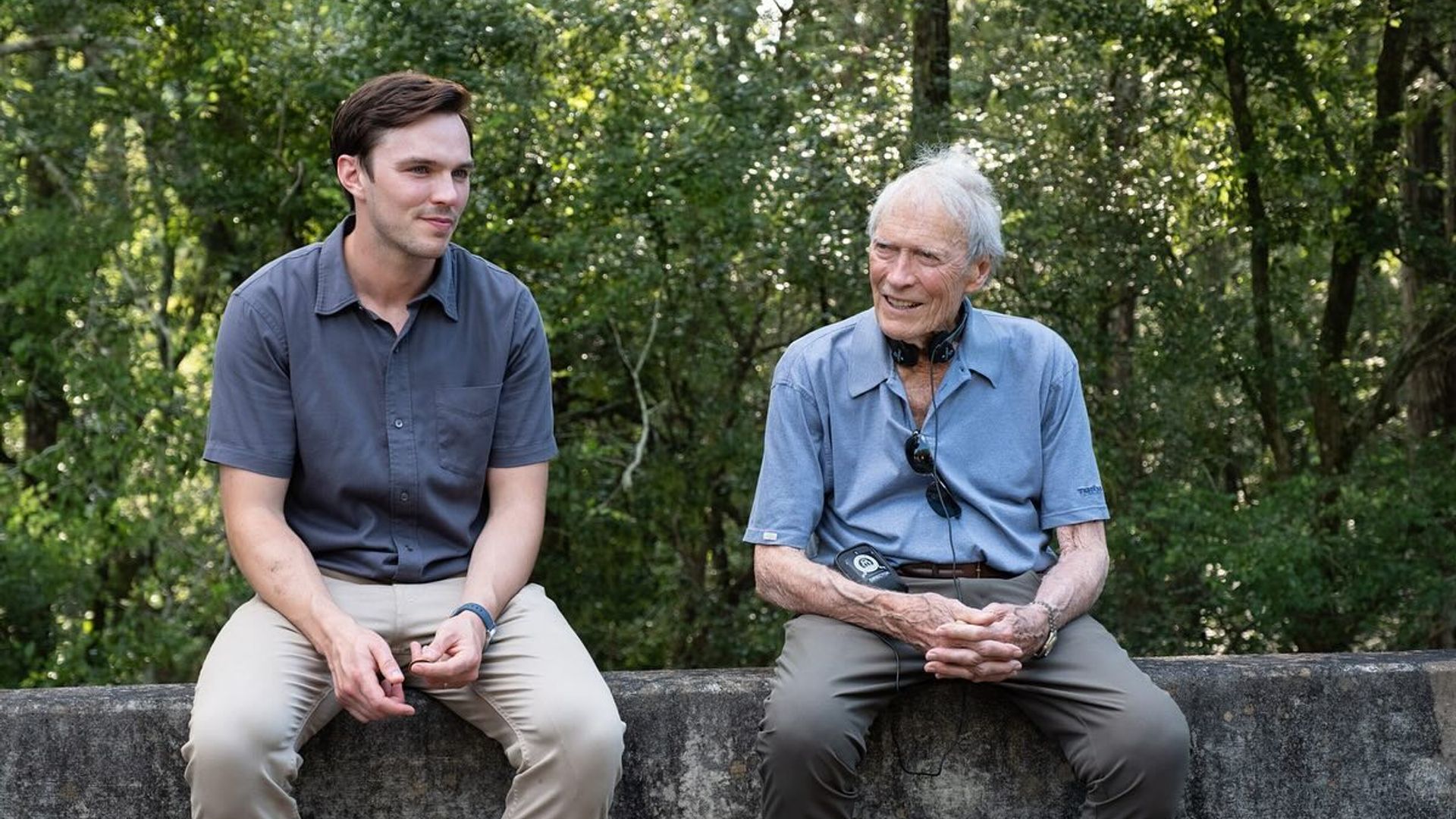 Nicholas Hoult i Clint Eastwood w casualowych ubraniach siedzą na betonowej barierze i rozmawiają na tle lasu