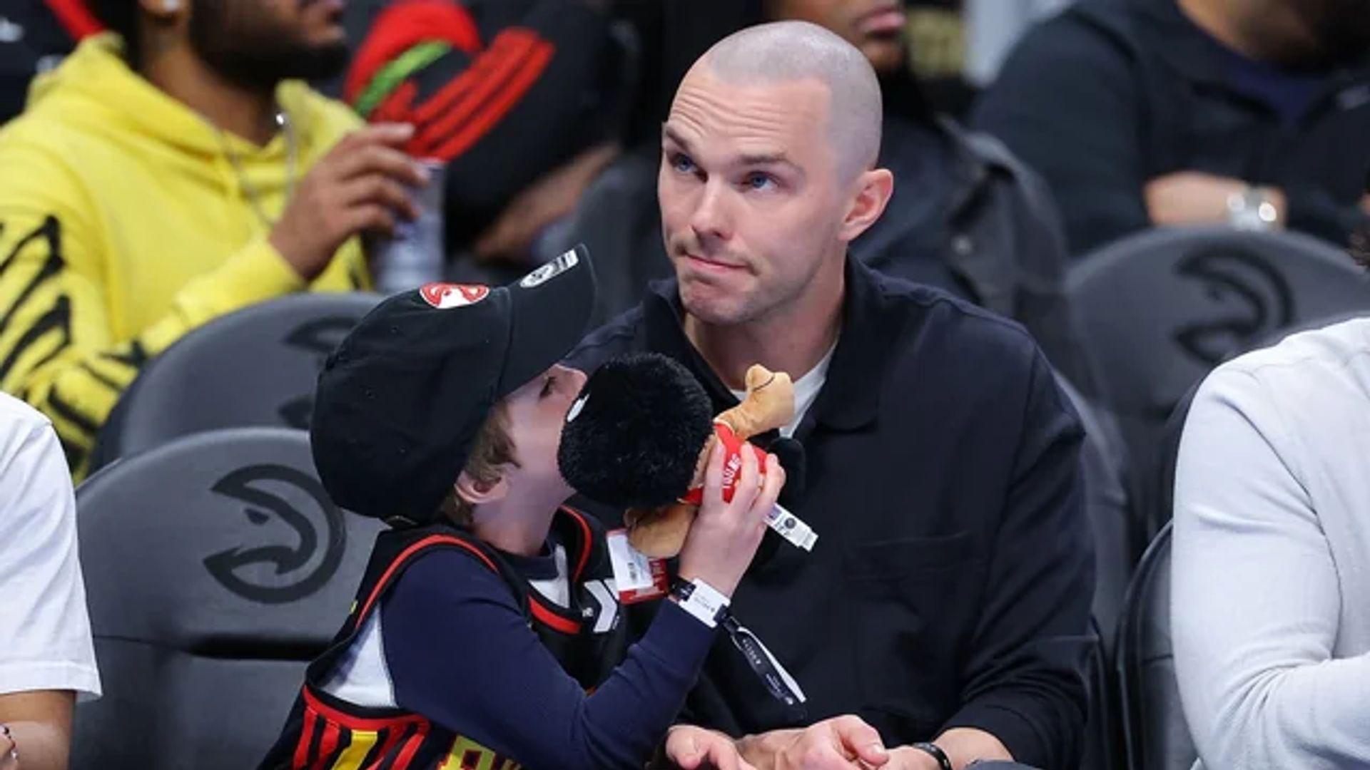 Nicholas Hoult siedzi na trybunach podczas meczu koszykówki obok swojego syna, który trzyma zabawkę
