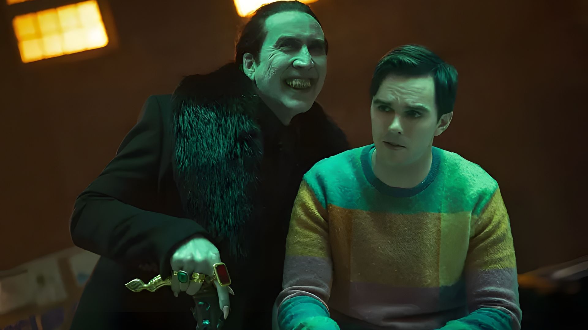 Nicolas Cage w czarnym ubraniu z pierścionkami groźnie góruje nad Nicholasem Houltem w kolorowym swetrze