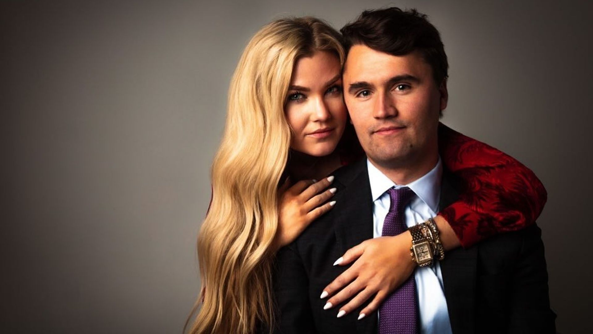 Charlie Kirk i Erica Frantzve przytulają się przed kamerą na ciemnym tle