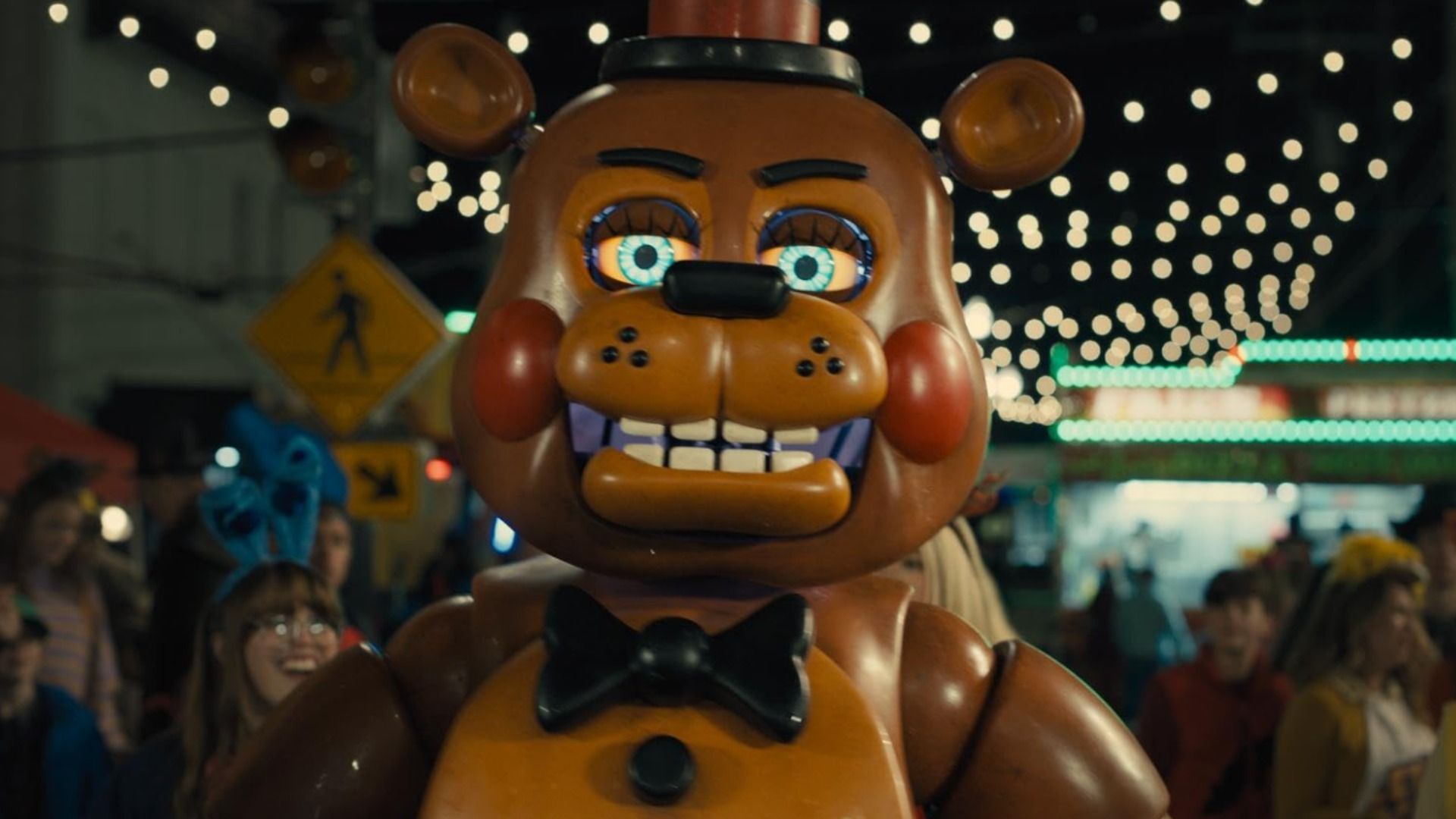 Animatronik w kształcie uśmiechniętego misia stojący w otoczeniu ludzi
