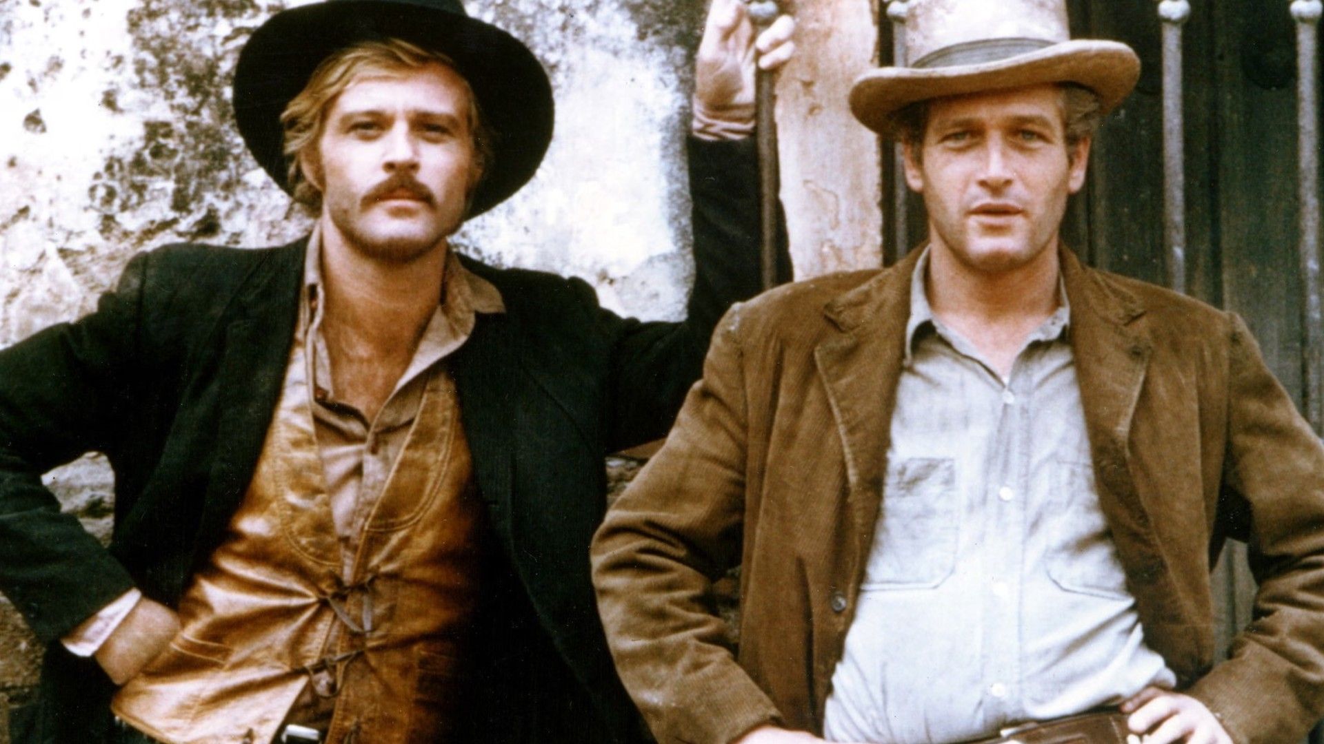 Robert Redford i Paul Newman w kowbojskich kapeluszach i kurtkach stojący obok siebie przy ścianie, pozujący do zdjęcia