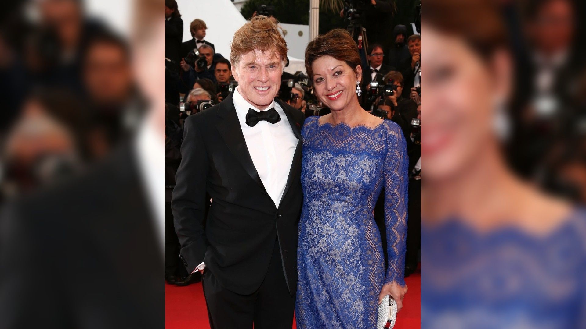 Robert Redford w smokingu i Sibylle Szaggars w niebieskiej koronkowej sukni pozują na czerwonym dywanie w otoczeniu fotografów