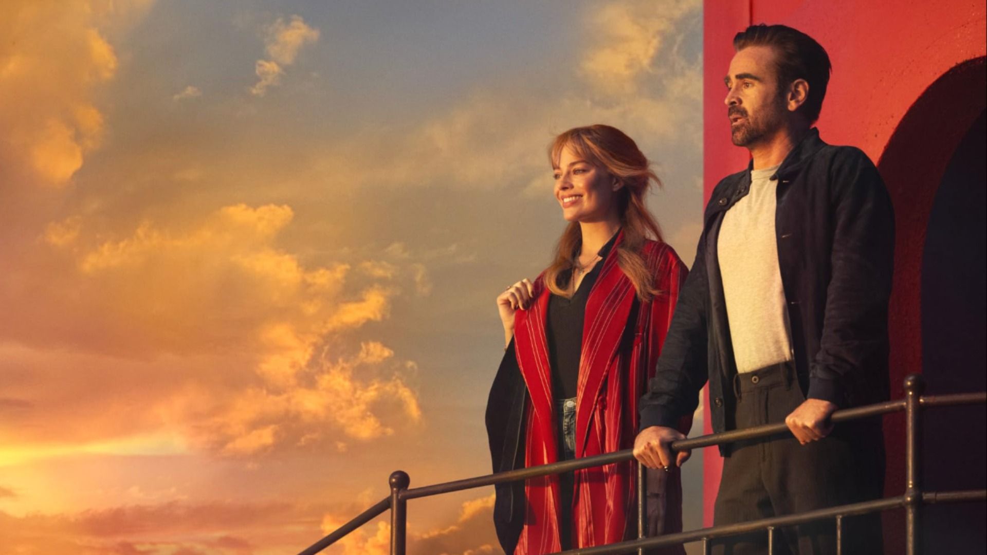 Aktorzy Margot Robbie i Colin Farrell stoją w casualowych ubraniach na pokładzie statku, obserwując zachód słońca