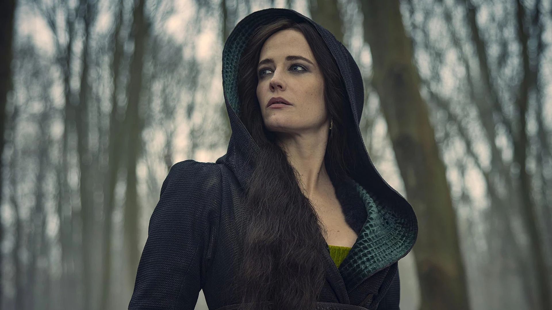 Eva Green w czarnej sukni z kapturem na tle zimowego lasu