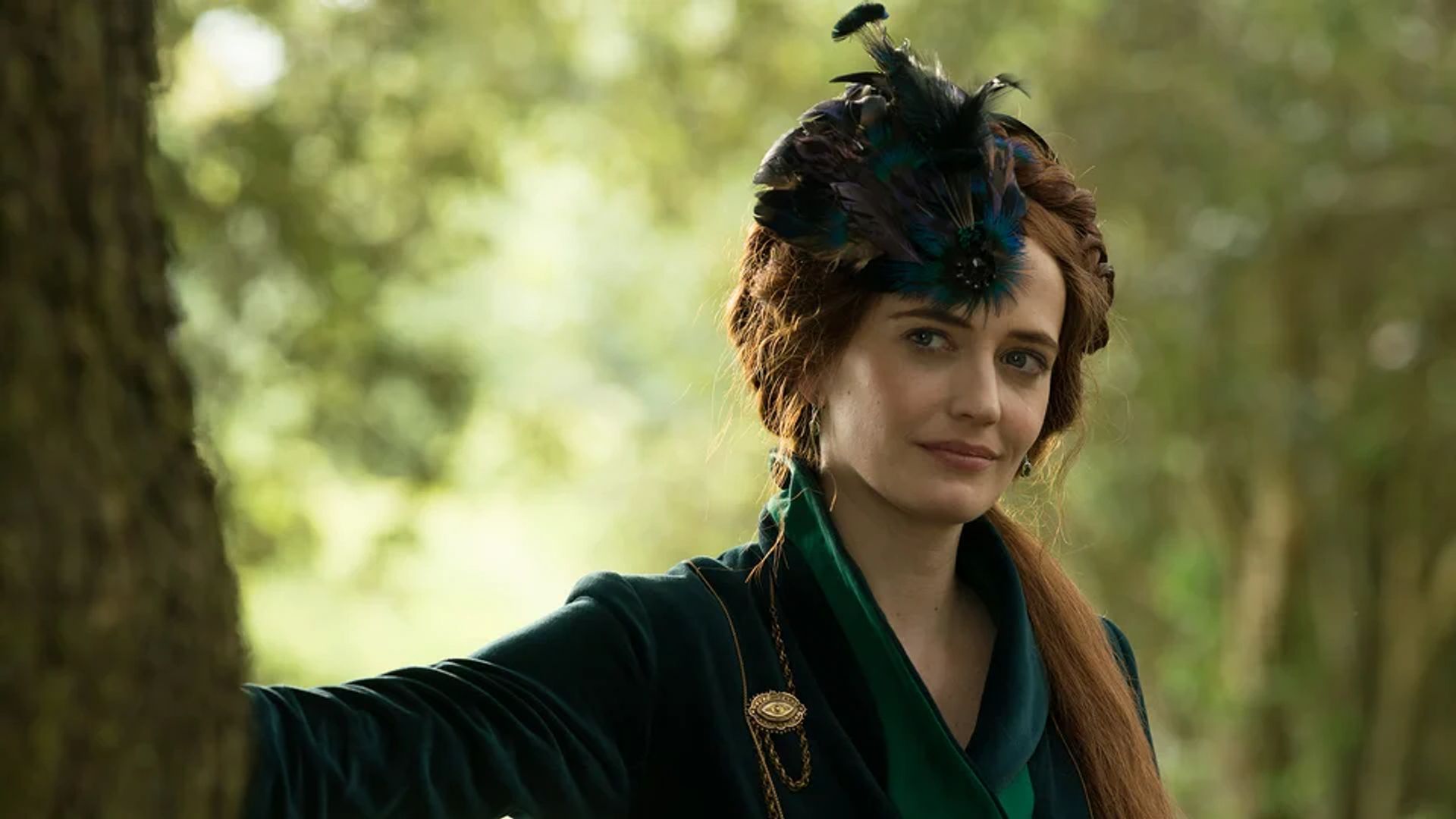 Eva Green w ciemnozielonym stroju z piórami na głowie stoi przy drzewie na tle lasu