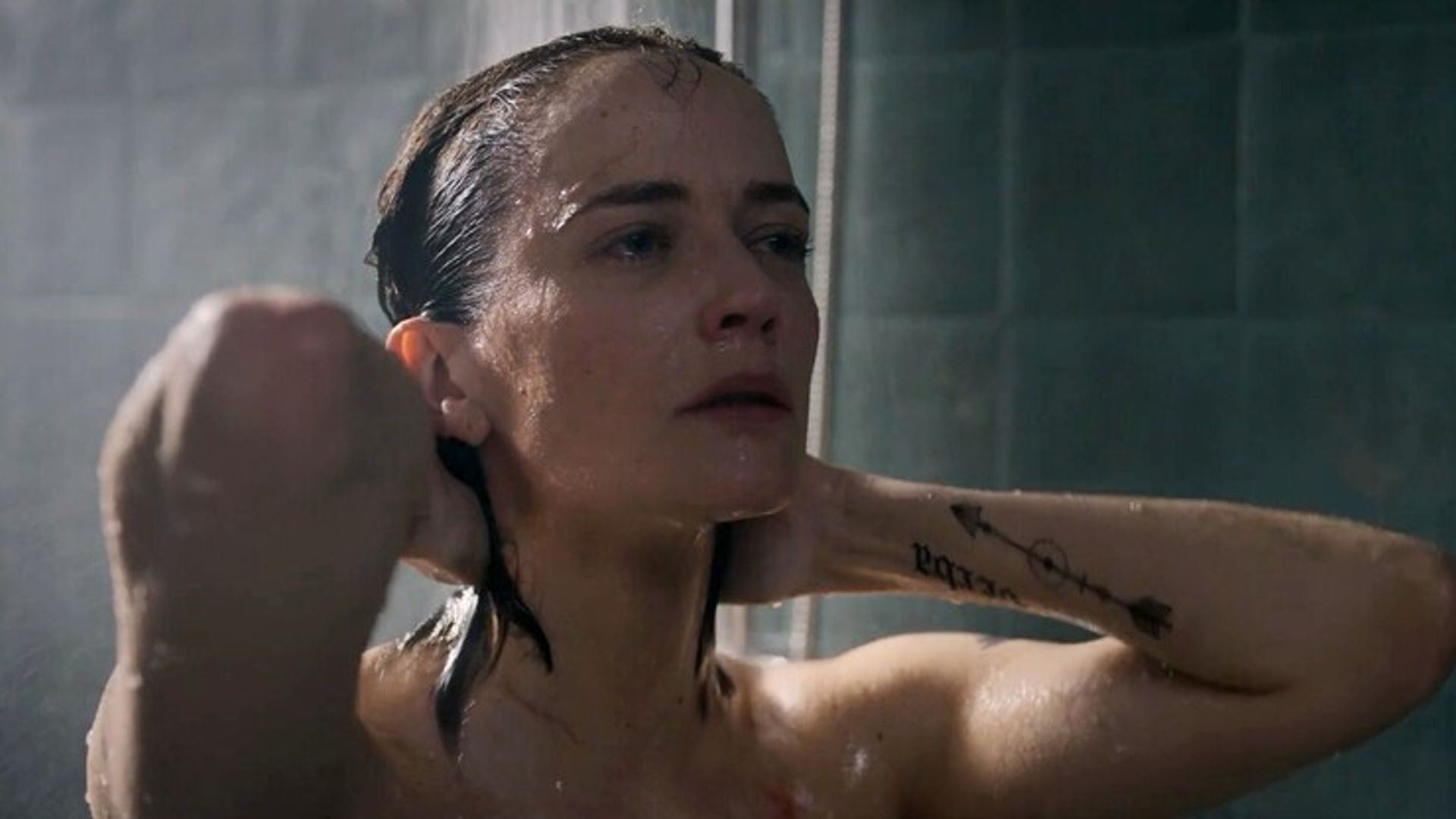 Eva Green z mokrymi włosami pod prysznicem, ręce za głową, widoczna tylko twarz i wytatuowane ramię