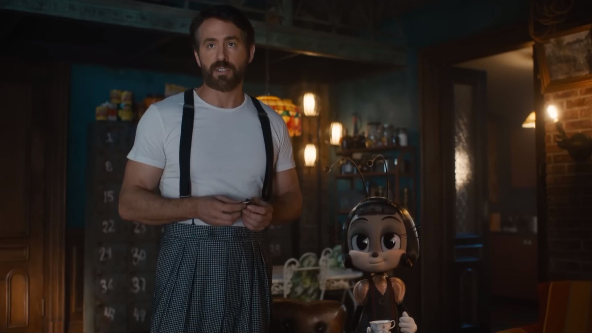 Ryan Reynolds w białej koszulce na szelkach stoi obok postaci kreskówkowej mrówki trzymającej filiżankę herbaty