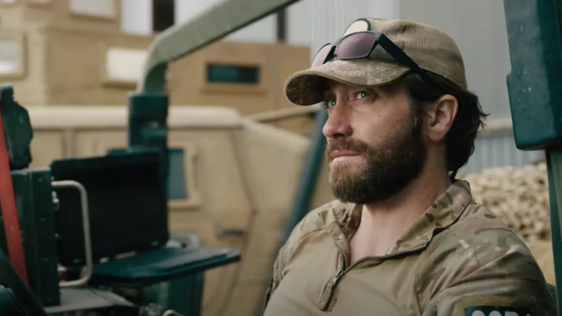 Jake Gyllenhaal w mundurze wojskowym i czapce z okularami na daszku siedzi patrząc w bok z poważnym wyrazem twarzy