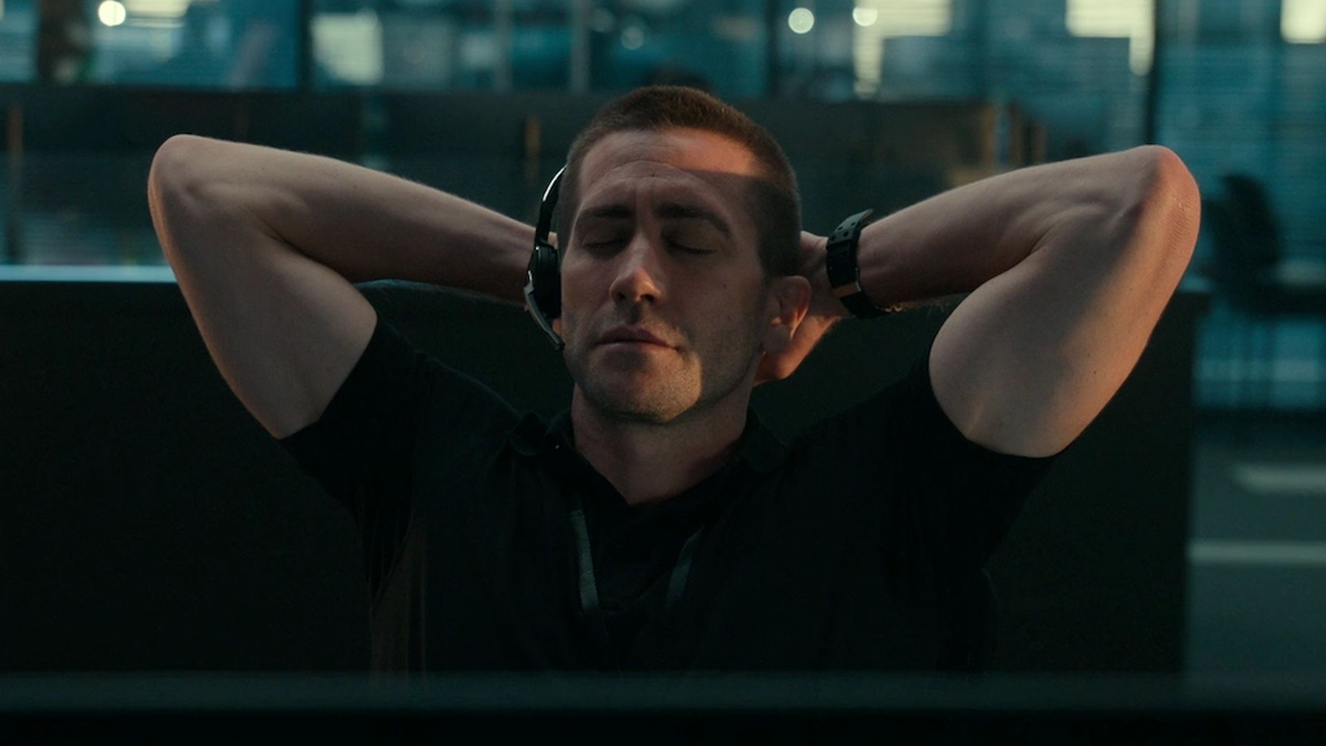 Jake Gyllenhaal w słuchawkach z mikrofonem siedzi z zamkniętymi oczami, ręce za głową